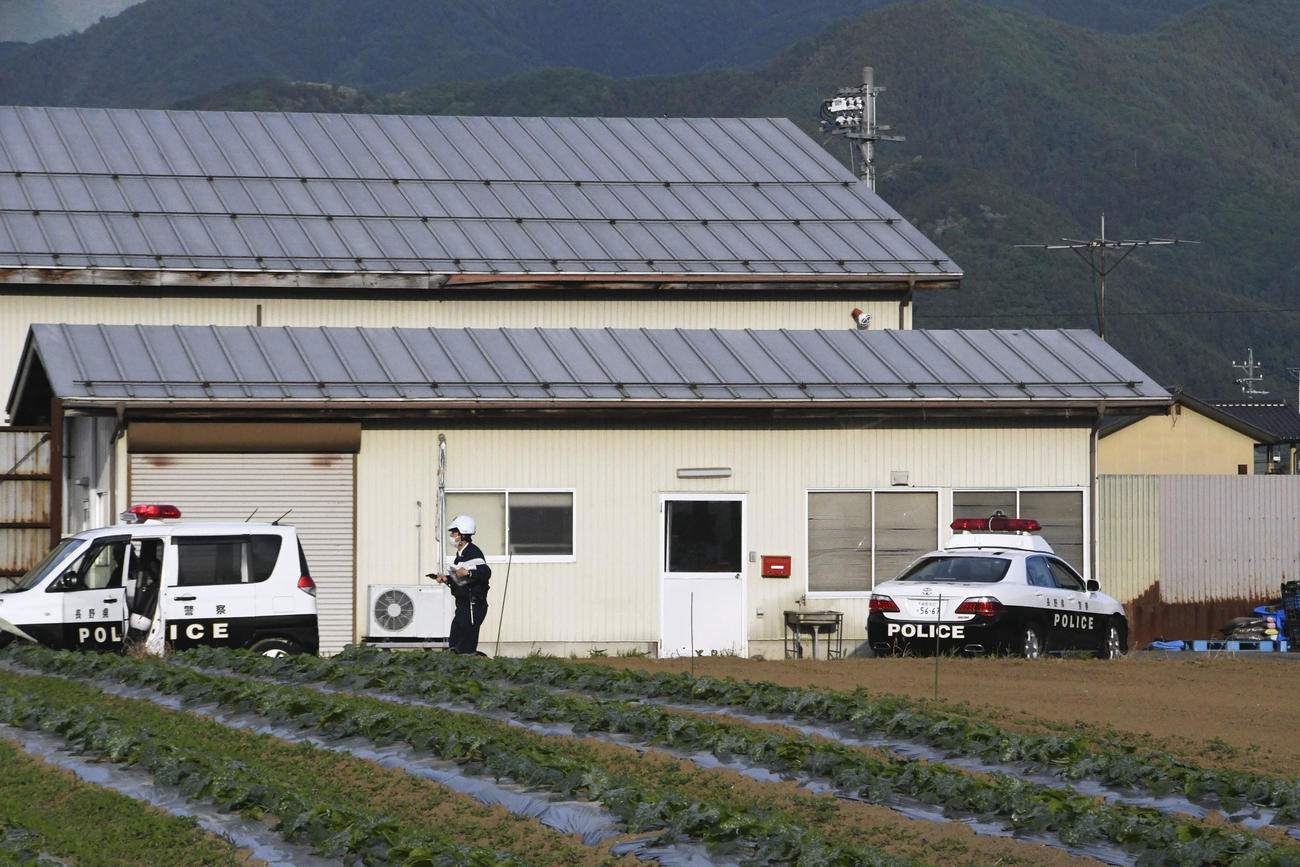 男が立てこもった建物の近くで警戒する捜査員ら。右側のパトカーからは、撃たれたとみられる警官が救急搬送された（共同）