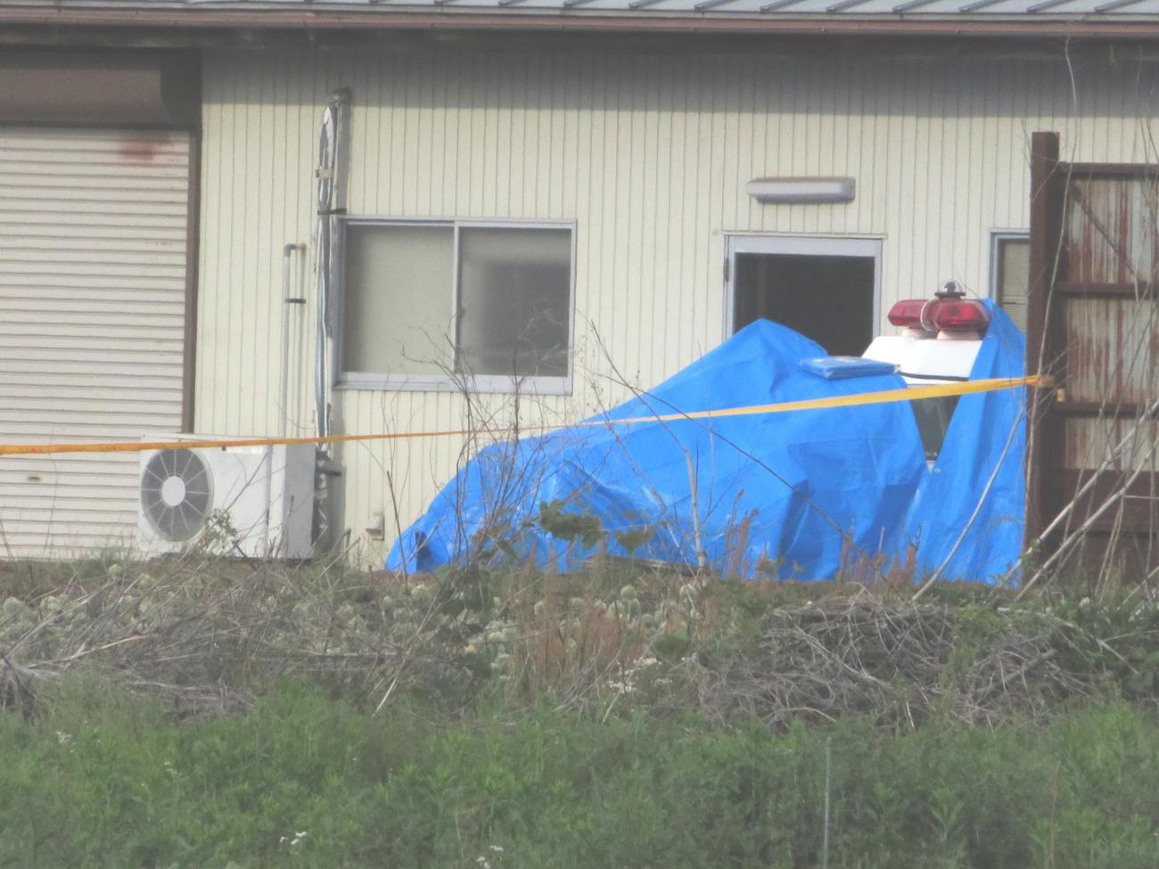 男が立てこもっていた住宅近くにある建物脇でシートがかけられたパトカー（撮影・寺沢卓）