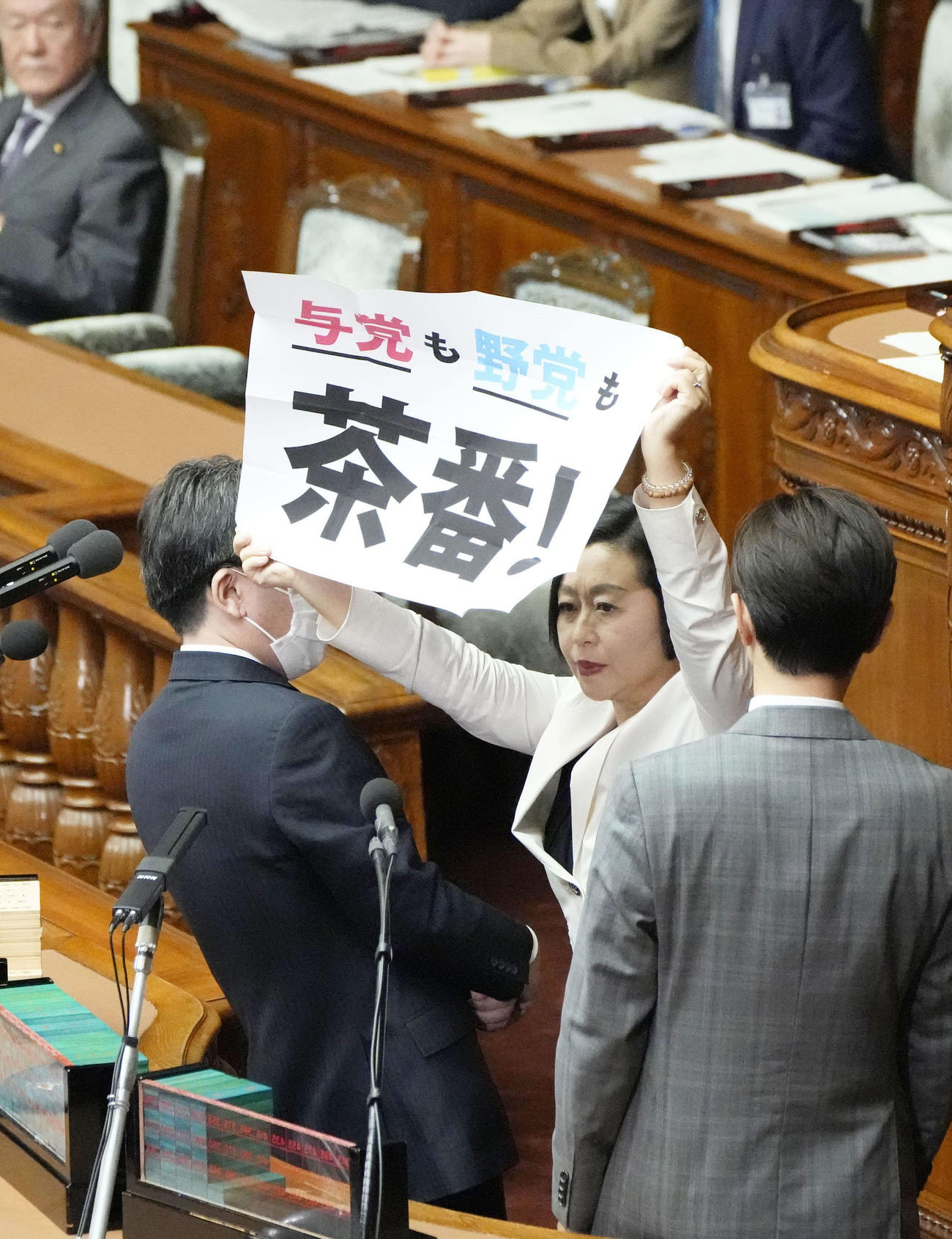 18日の衆院本会議で「与党も野党も茶番！」と書かれた紙を持って壇上で広げるれいわ新選組の櫛渕万里共同代表（共同）