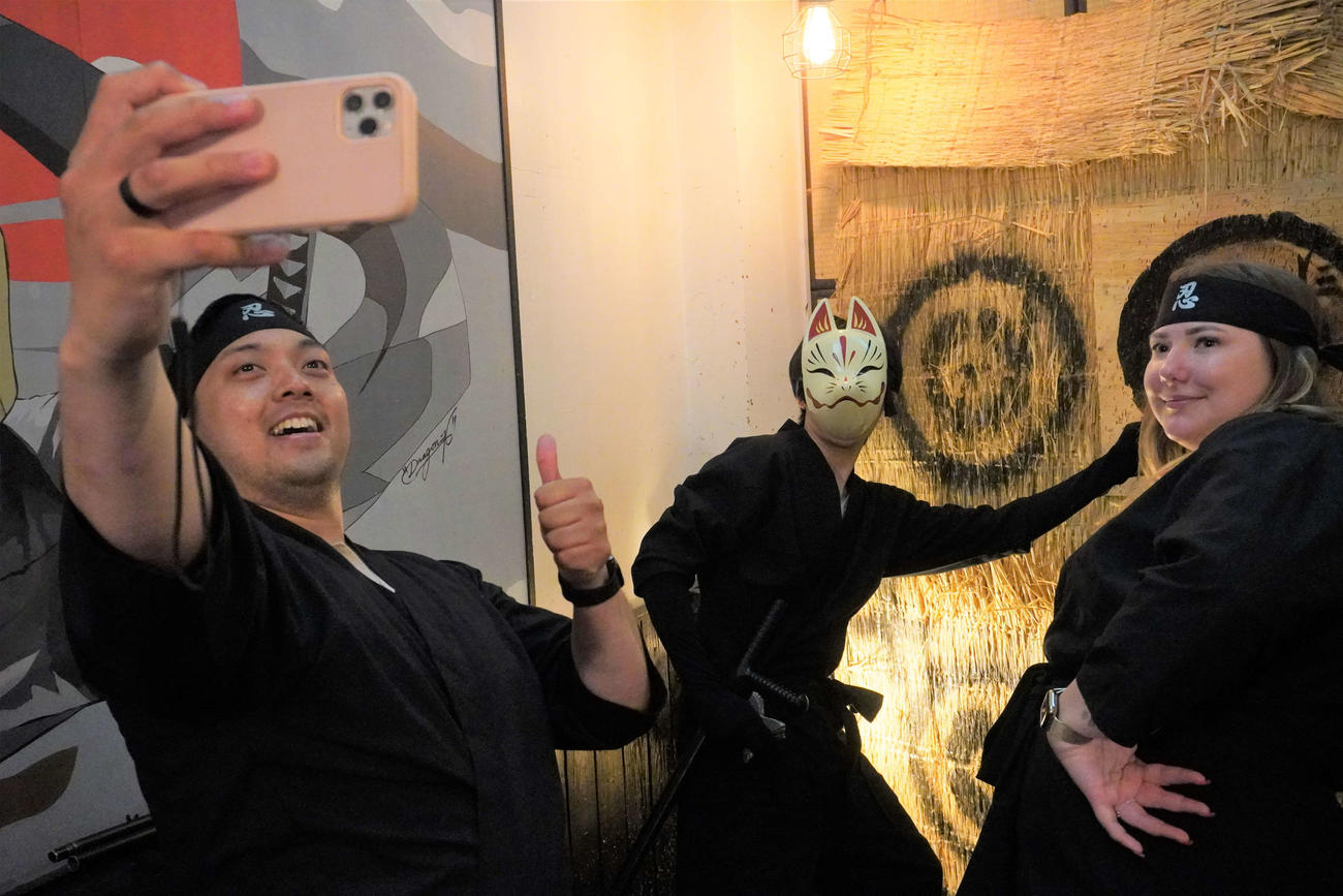 忍者カフェでスタッフの忍者（中央）と記念撮影をするアーサーさん（左）とドミニカさん（撮影・沢田直人）