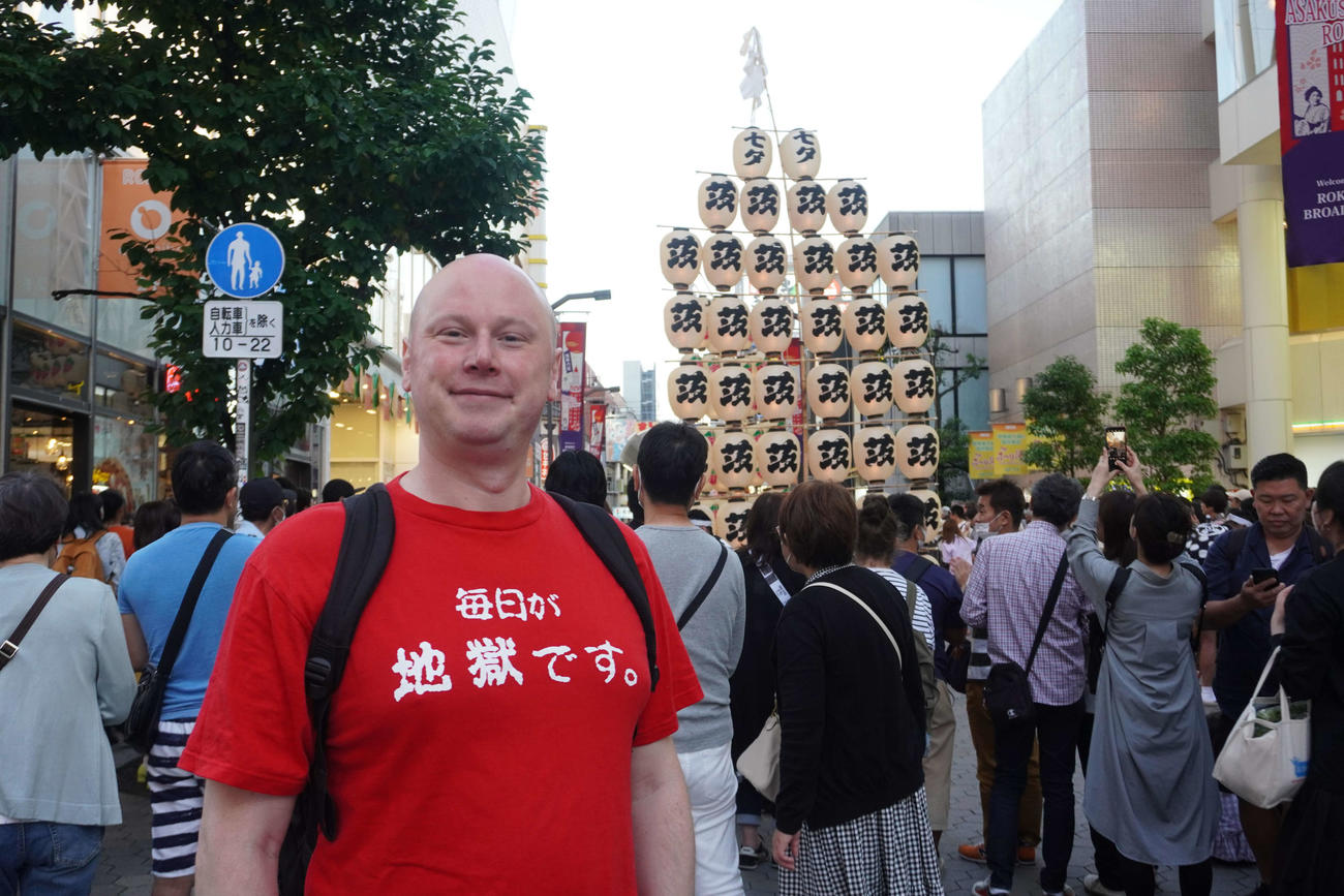 「毎日が地獄です」と書かれたユニークなTシャツを着て笑顔を見せるエリックさん（撮影・沢田直人）