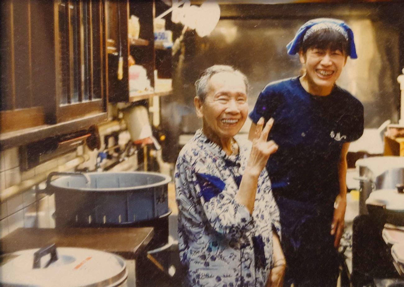 初代女将の幸子さんと厨房（ちゅうぼう）で記念写真（提供・石橋悦子さん）