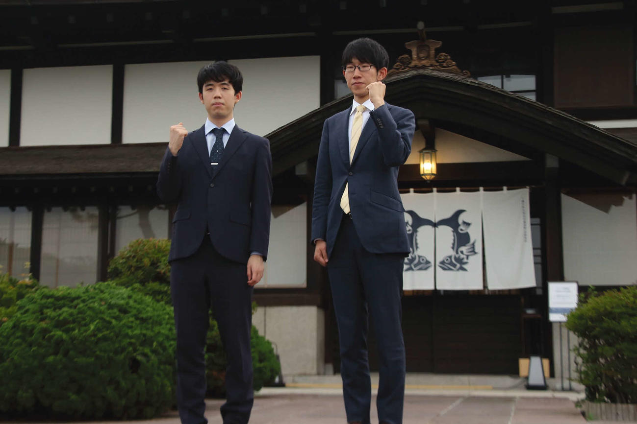 24日、対局場となる「銀鱗荘」の前でガッツポーズを作る藤井聡太王位（左）と佐々木大地七段（右＝日本将棋連盟提供）