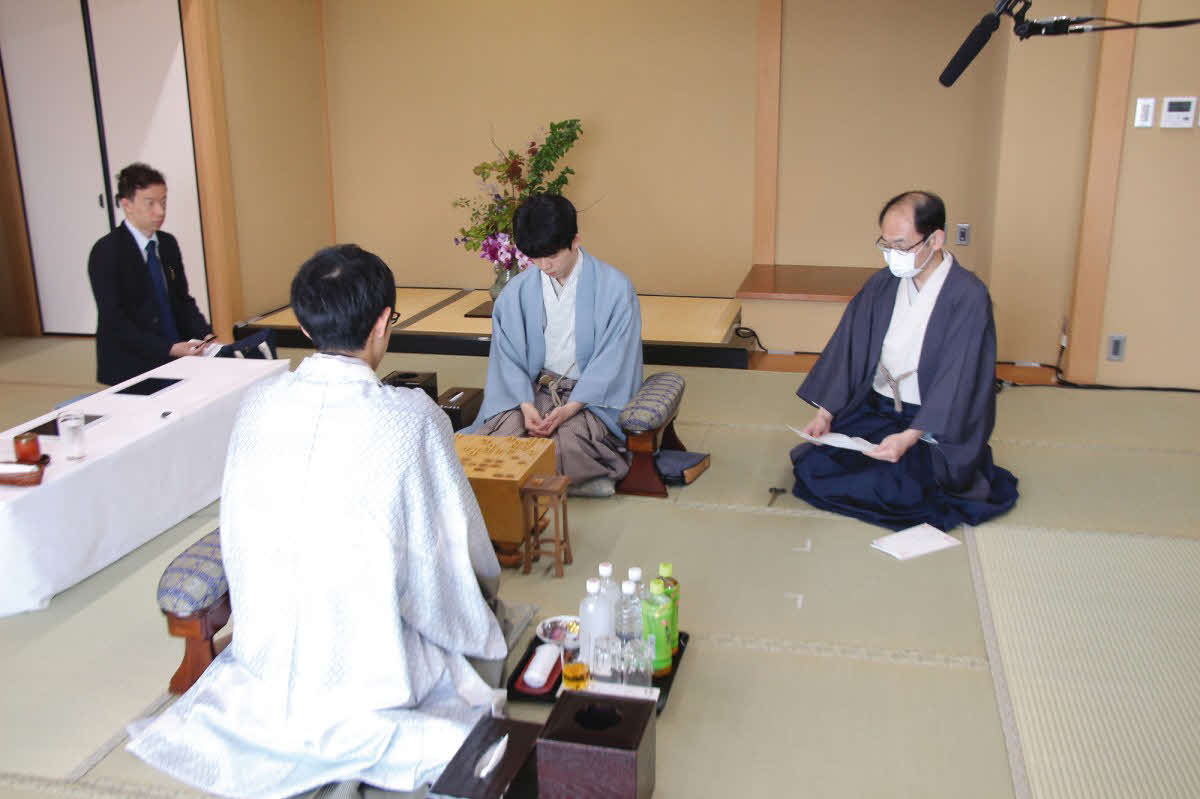 立会人の木村一基九段（右）が封じ手を開封して佐々木大地七段（左）が藤井聡太王位（中央）に挑戦する王位戦第3局2日目が再開（日本将棋連盟提供）