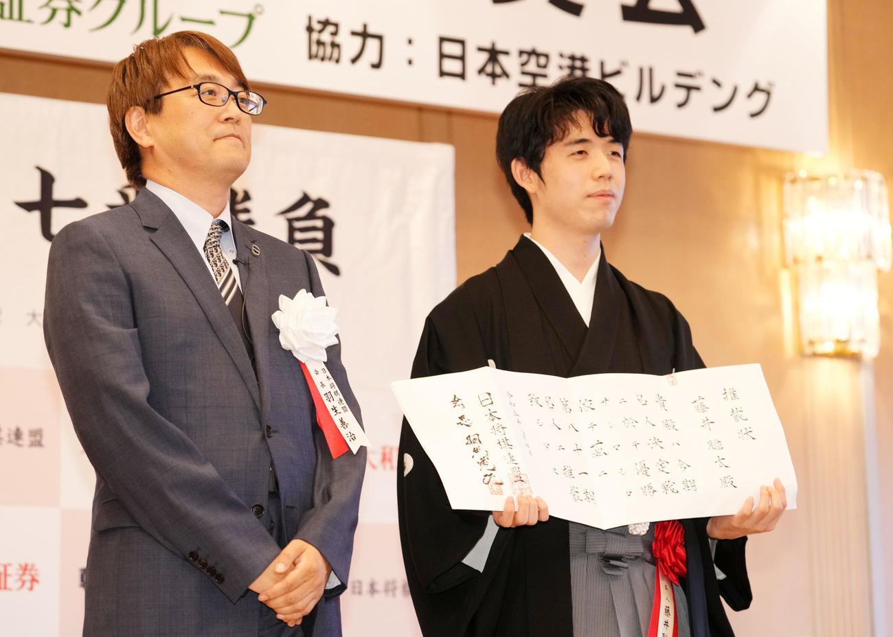 推戴状を手に笑顔を見せる藤井聡太名人。左は羽生善治会長（撮影・横山健太）