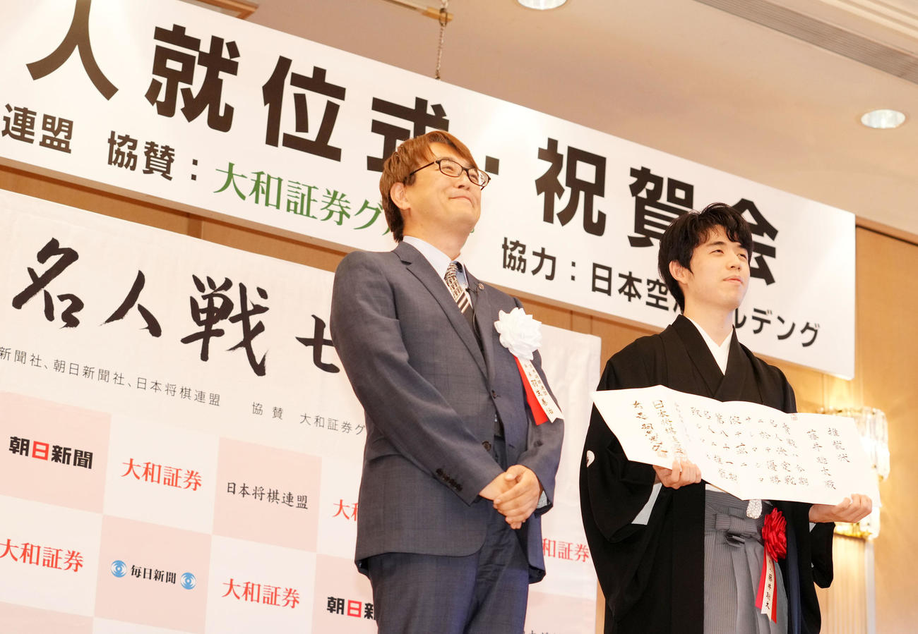 推戴状を手に笑顔を見せる藤井聡太名人。左は羽生善治会長（撮影・横山健太）