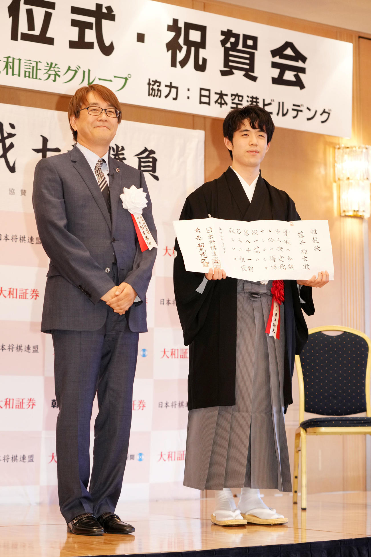 推戴状を手に笑顔を見せる藤井聡太名人。左は羽生善治会長（撮影・横山健太）
