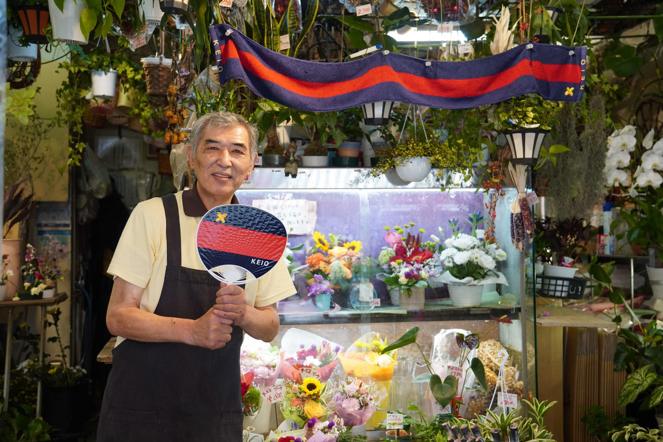 慶応のうちわとタオルを掲げ応援する生花店「二宮花園」の二宮陸次代表取締役（撮影・沢田直人）
