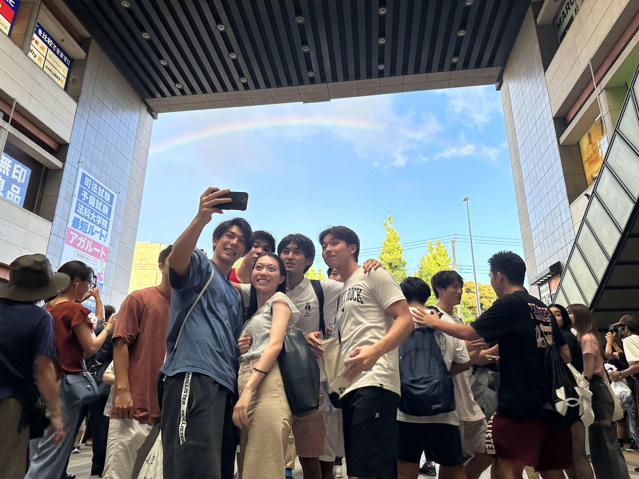 慶応野球部の優勝後、東の空にかかった虹をバックに東急・日吉駅で写真を撮る慶応大の学生ら（撮影・沢田直人）