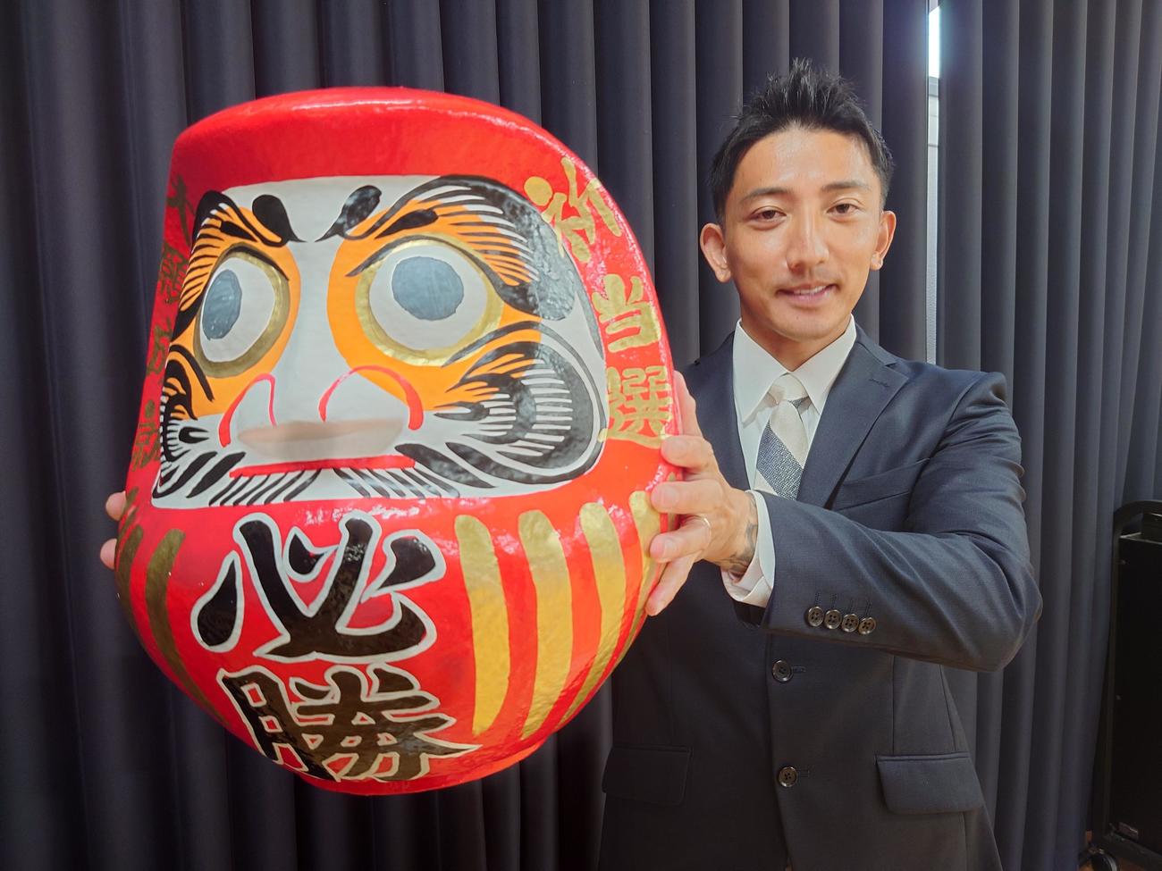 当選一夜明け会見前で両目を入れたダルマを持つ後藤祐樹氏（撮影・寺沢卓）