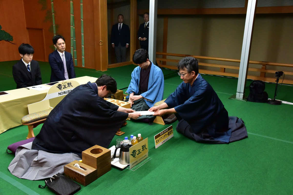 タイトル戦初登場の伊藤七段（左）は封じ手の入った封筒を立会人の佐藤九段（右）に手渡す。中央は藤井竜王（日本将棋連盟提供）