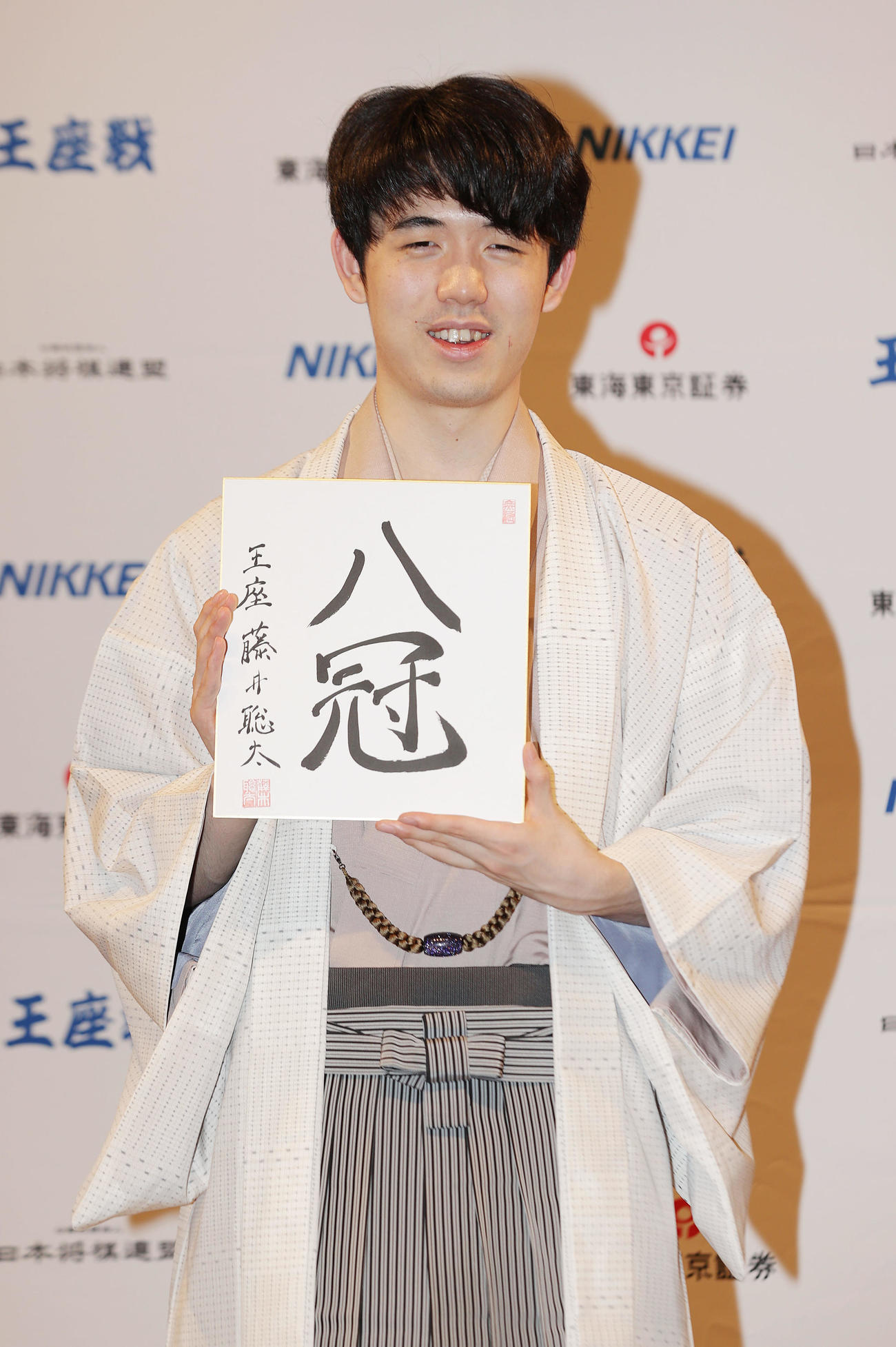 「8冠」と記した色紙を手に笑顔を見せる藤井新王座（撮影・前田充）