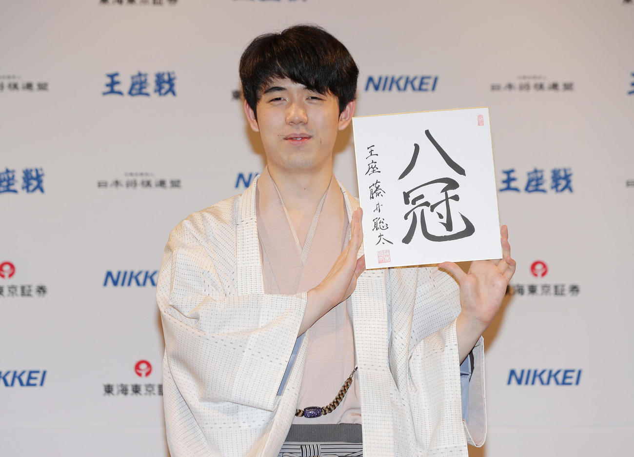 「8冠」と記した色紙を手に笑顔を見せる藤井新王座（撮影・前田充）