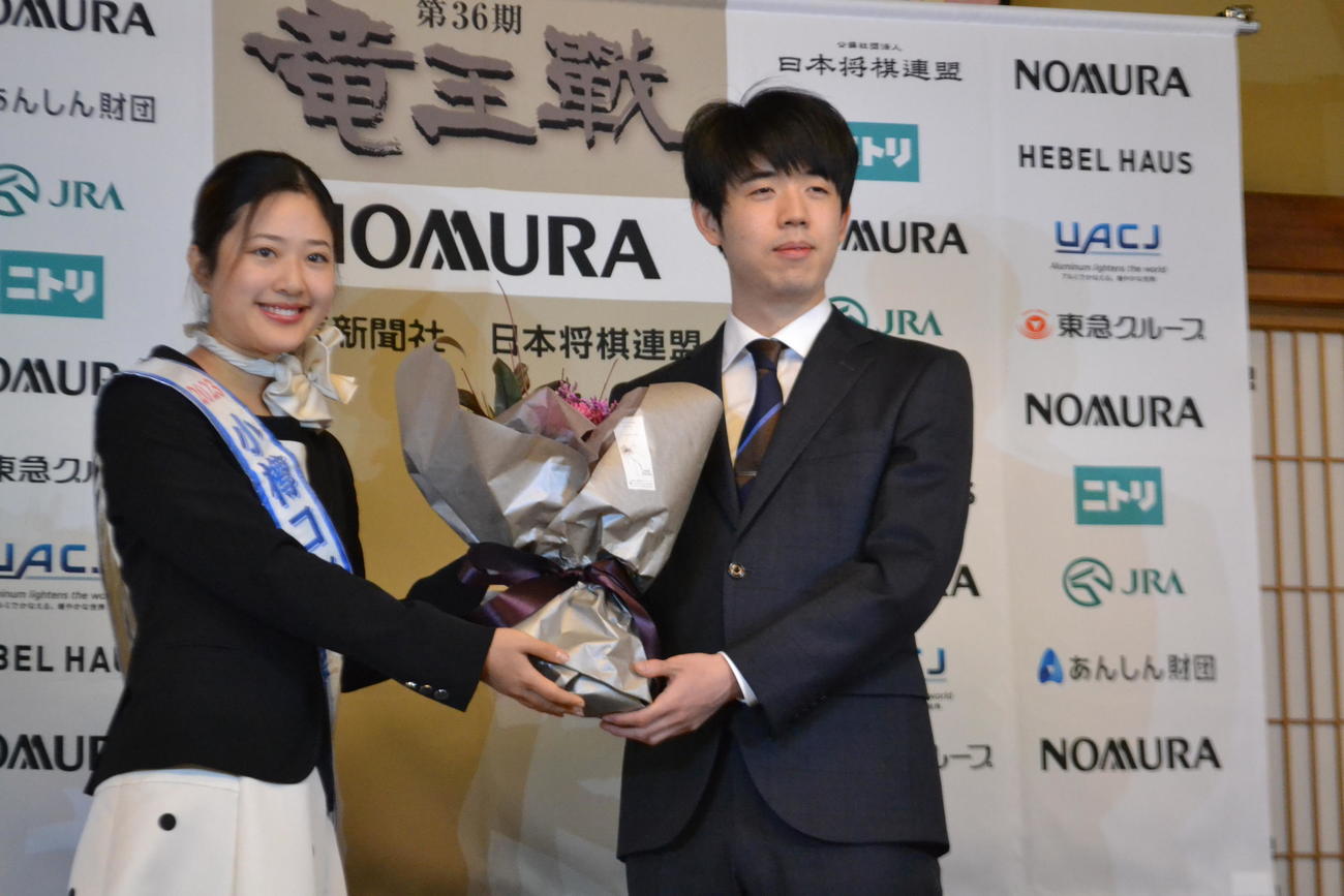 一夜明け会見の最初に「小樽コンシェルジュ」の富樫凛子さん（左）から花束を贈呈された藤井聡太竜王