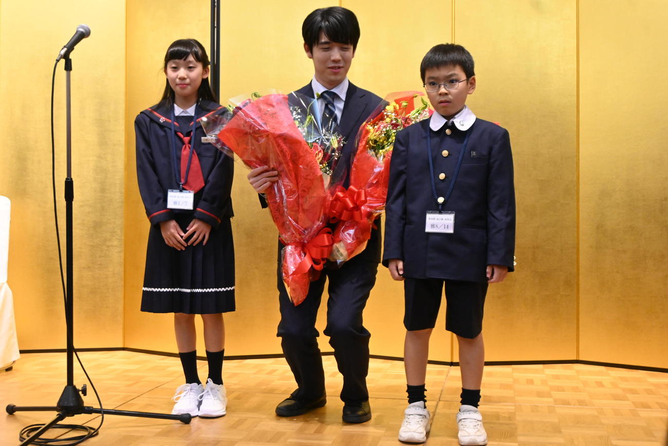花束を贈呈された藤井聡太竜王は、子どもたちと背丈を合わせるように少ししゃがんで記念撮影（撮影・松浦隆司）