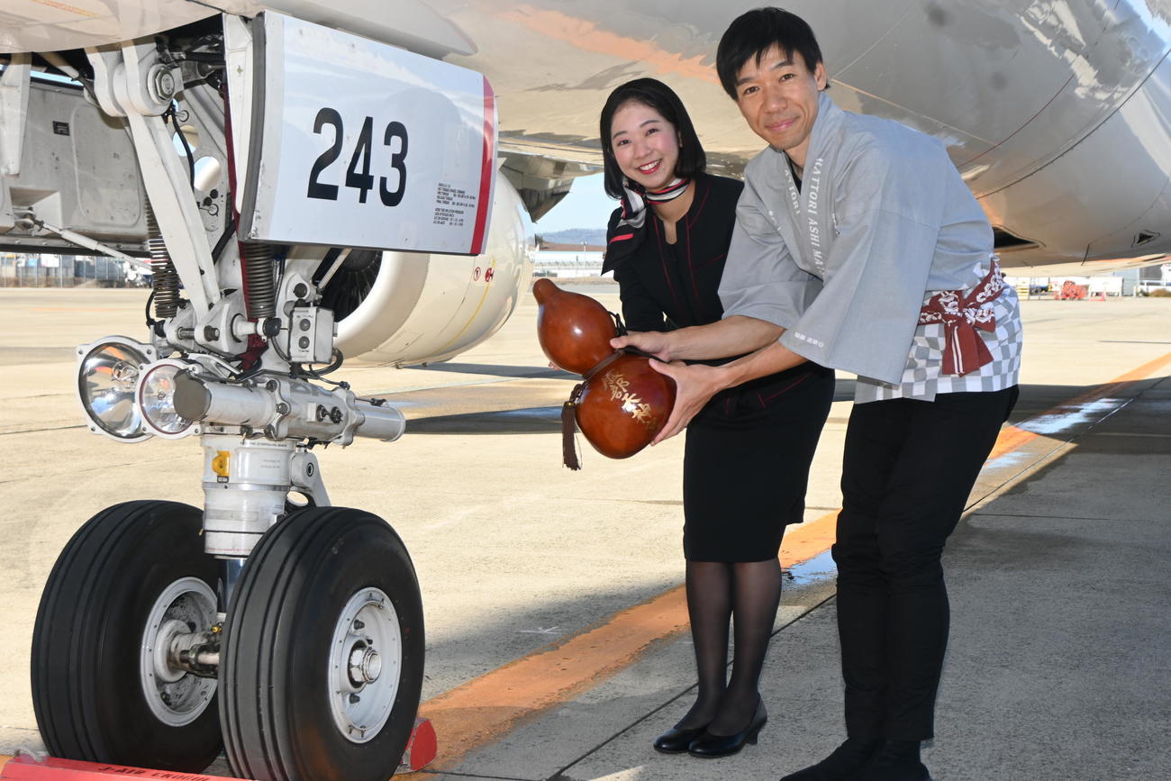 服部天神宮の「ご神水」をランディングギア（足）にかける客室乗務員の森川詩織さん（左）、アドベンチャーランナーの北田雄夫さん（撮影・松浦隆司）