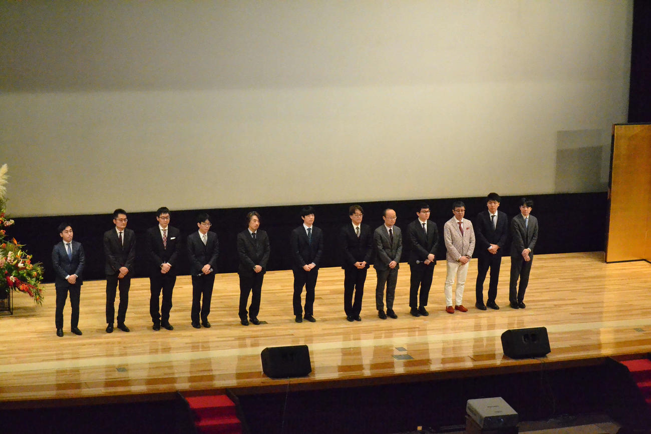 開会式で登壇した菅井竜也八段、稲葉陽八段、山崎隆之八段、豊島将之九段、久保利明九段、藤井聡太8冠、羽生善治九段、渡辺明九段、永瀬拓矢九段、野月浩貴八段、増田康宏七段、青嶋未来六段（左から）
