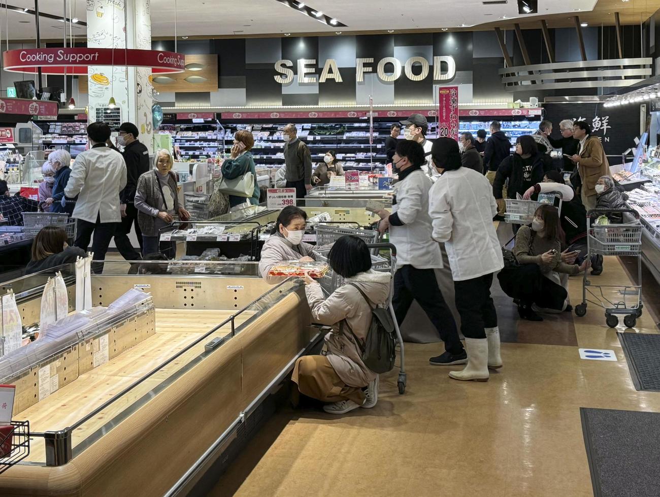 富山市の大型商業施設のスーパーで地震に遭い、床に座る買い物客ら＝1日午後4時12分（共同）
