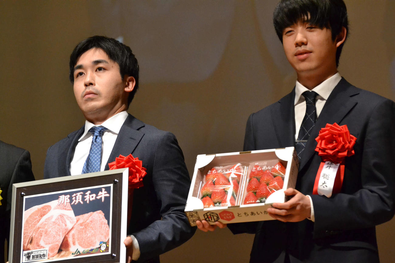 記念品贈呈で栃木の特産品を手にする菅井竜也八段（左）と藤井聡太王将（右）