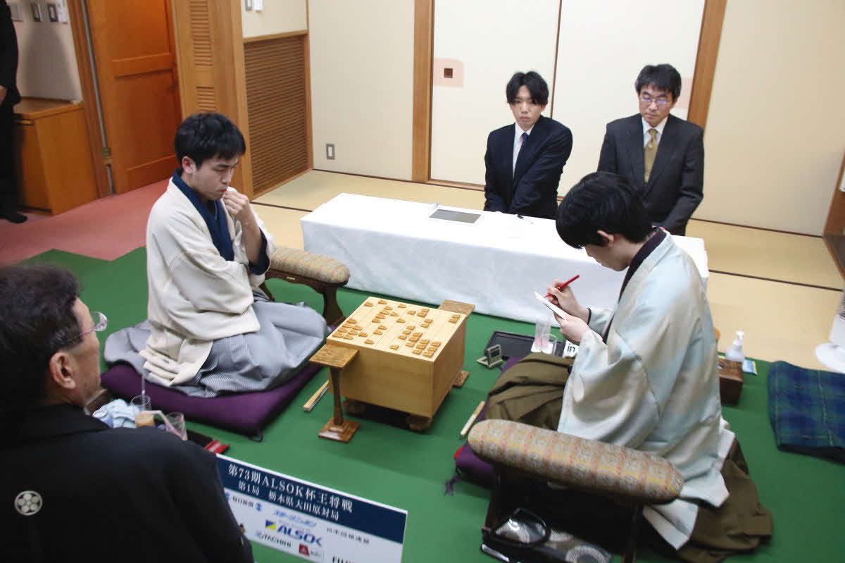 菅井竜也八段（左）が封じ手を入れた封筒に署名する藤井聡太王将（右、日本将棋連盟提供）