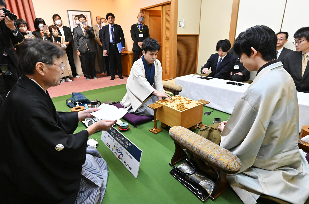 第73期王将戦七番勝負第1局の2日目、立会の塚田九段（左）が開封した封じ手を指す挑戦者の菅井八段（中央）。右は藤井王将（代表撮影）