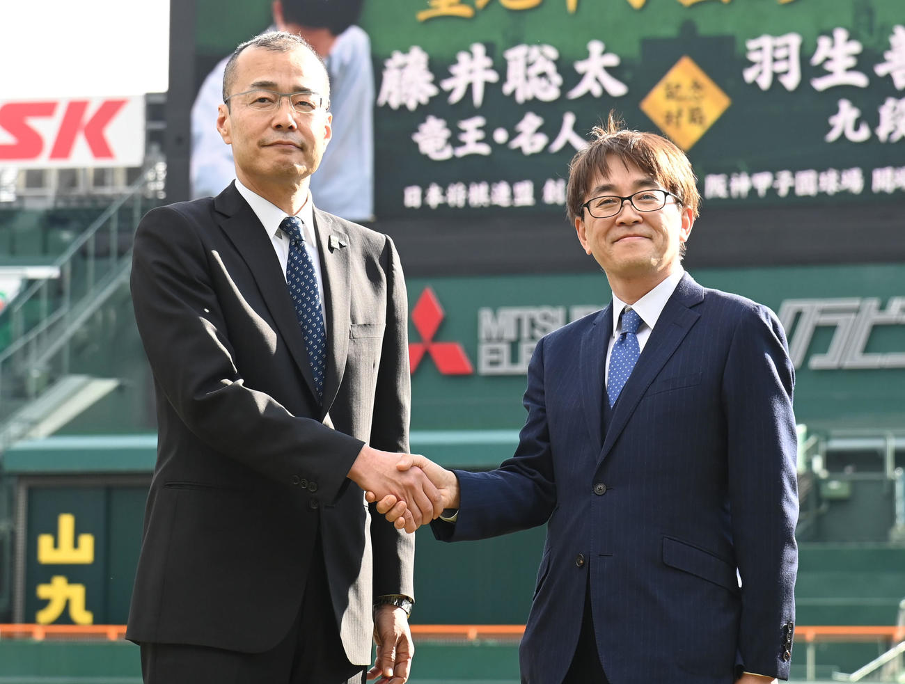 甲子園球場で握手をする（左から）阪神甲子園球場長・向井格郎、日本将棋連盟会長・羽生善治（撮影・石井愛子）