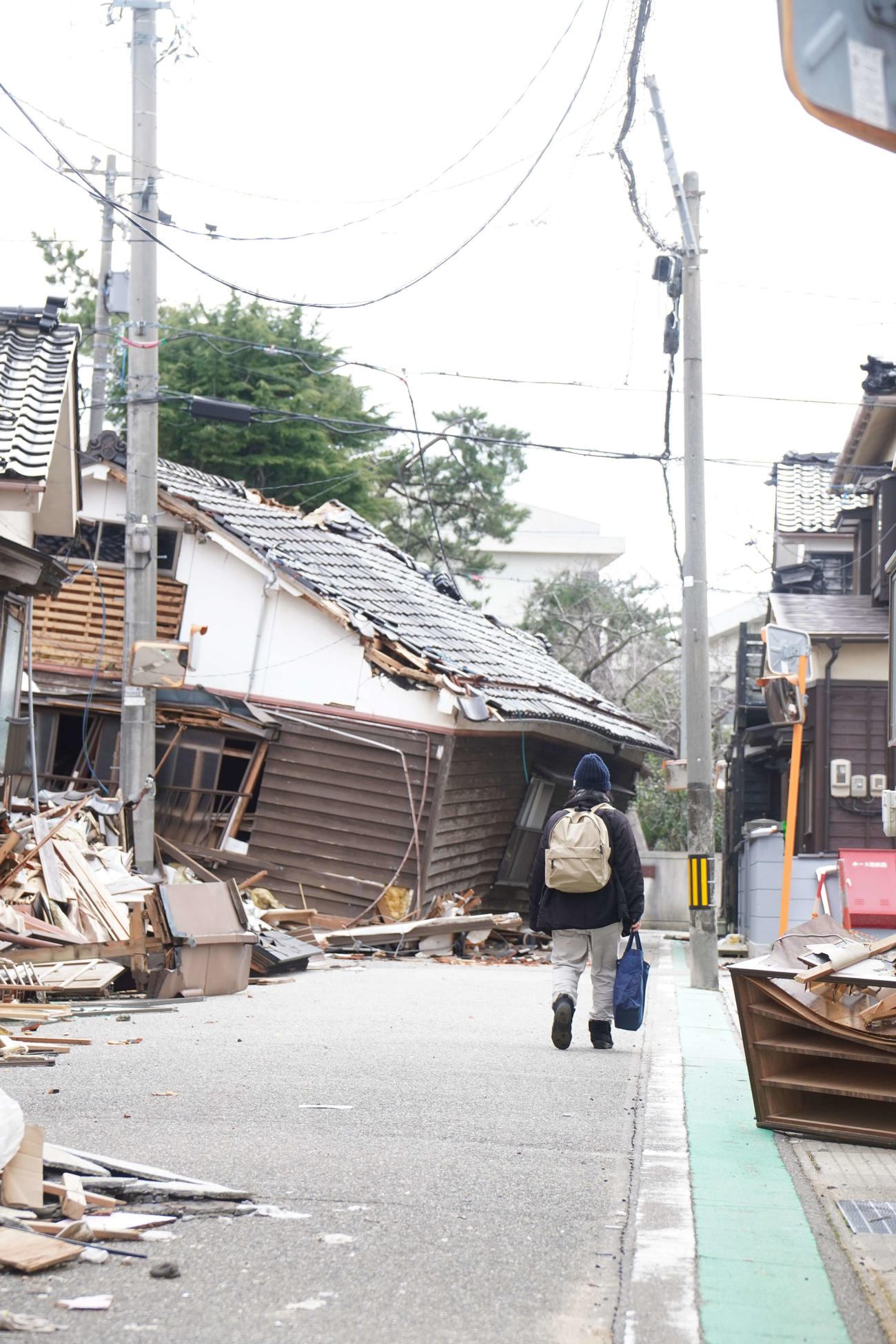 石川県輪島市で地震の影響で崩れた家屋の横を歩く女性（撮影・沢田直人）