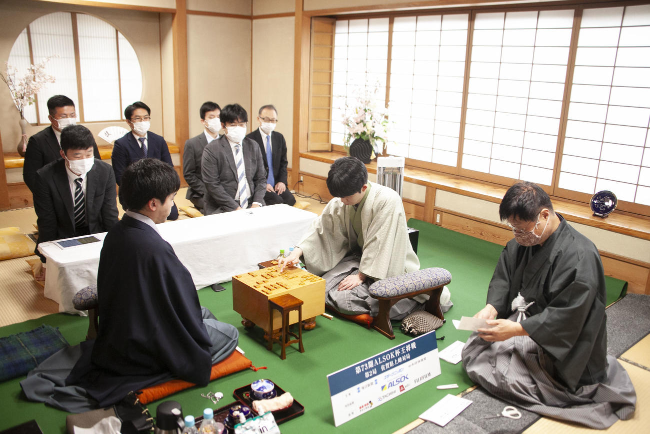 封じ手の読み上げる立会人の小林健二九段（右）、藤井聡太王将（中央）、菅井竜也八段（左）（日本将棋連盟提供）