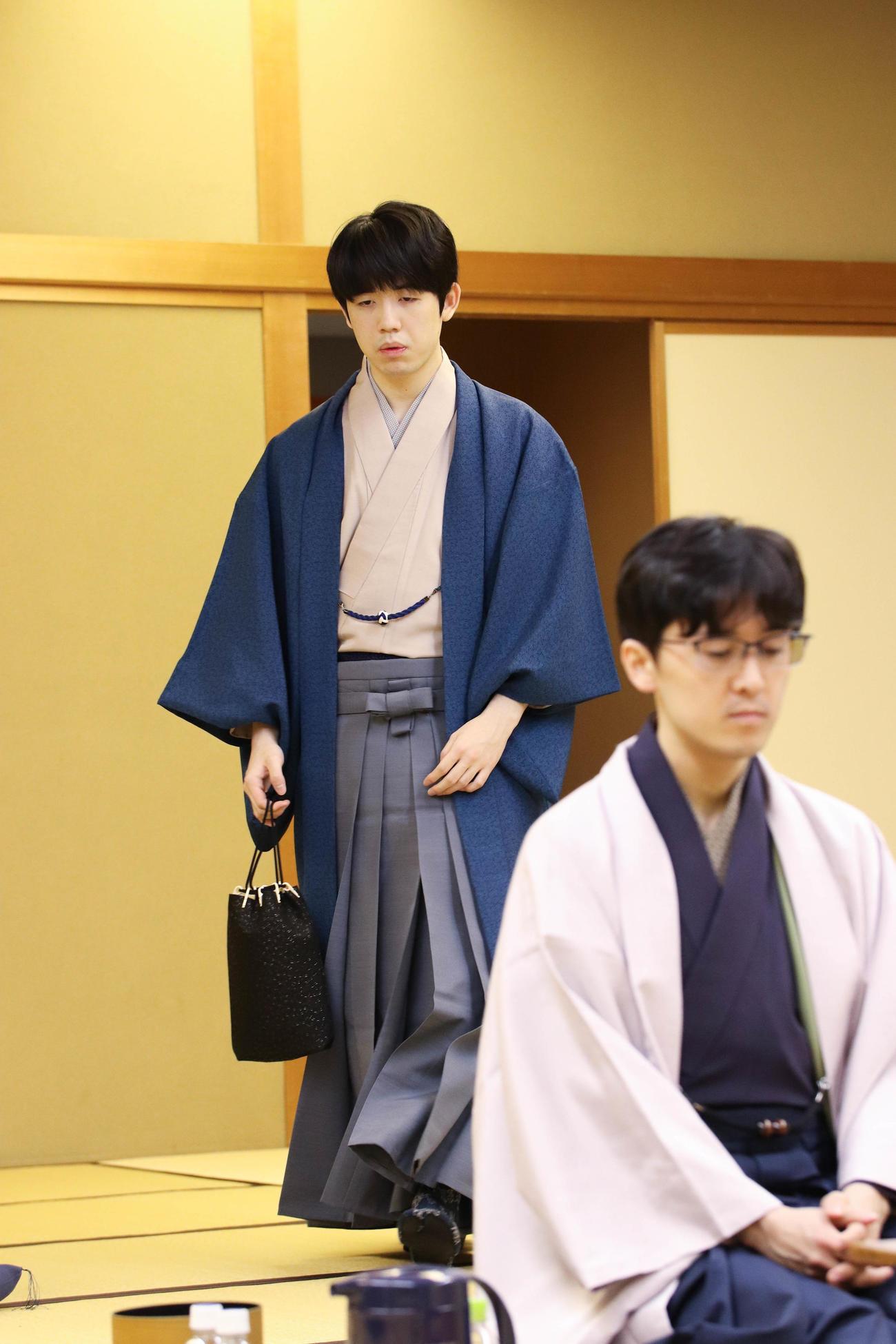 棋王戦5番勝負第1局の対局室に入室する藤井聡太棋王、手前は伊藤匠九段（日本将棋連盟提供）