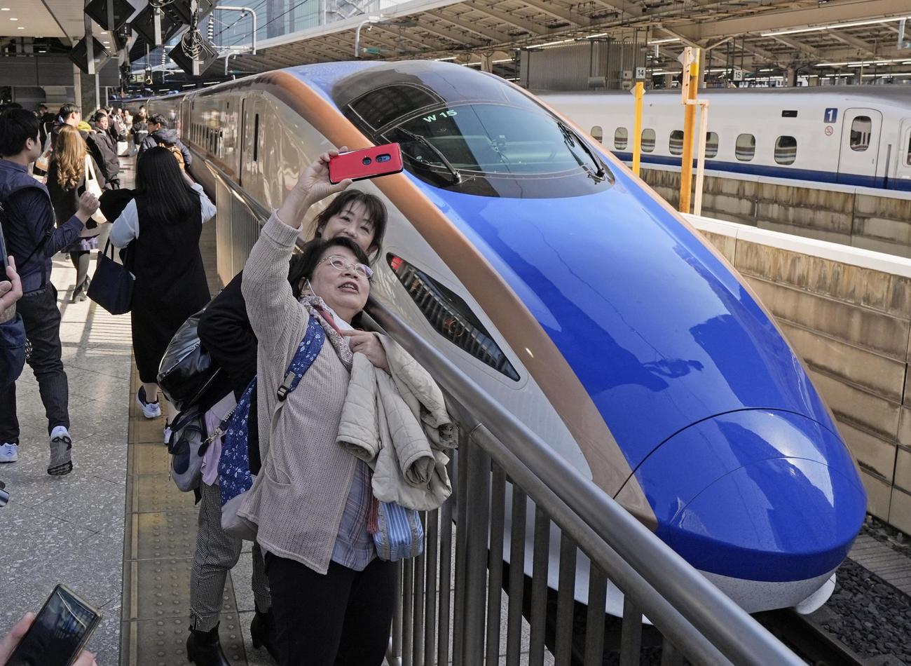 北陸新幹線の金沢－敦賀間が延伸開業し、JR東京駅に到着した敦賀発の一番列車「かがやき502号」と記念撮影する敦賀からの乗客ら（共同）
