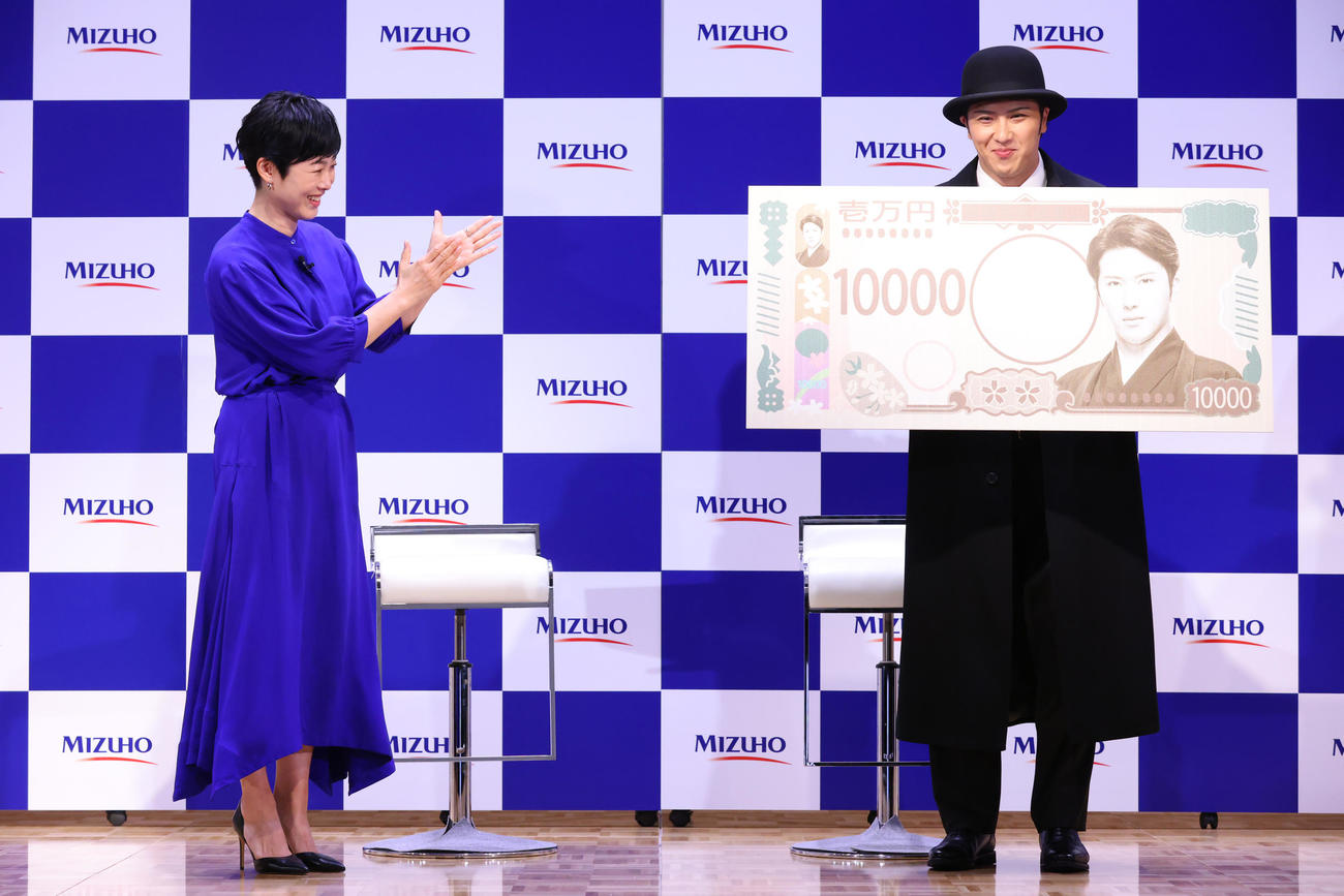 自身が肖像になった特大1万円札を手にする尾上松也（右）。左は有働由美子