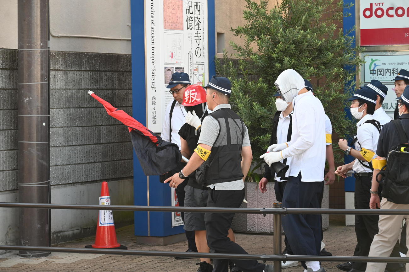 現場となった奈良・大和西大寺駅前に設置された献花台の近くで赤いヘルメットの男性と上半身白ずくめの男性が警察官をもみ合いになり騒然（撮影・松浦隆司）