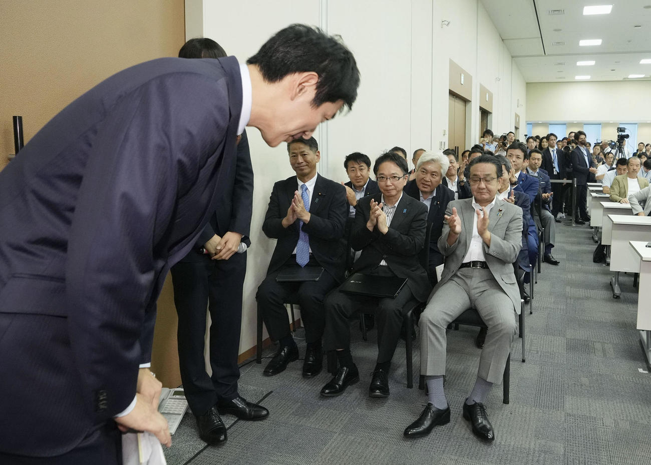 自民党総裁選への立候補表明の記者会見を終え、一礼して引き揚げる小林前経済安保相。記者席の隣や背後で支援の国会議員らが見守った＝19日午後、国会（共同）