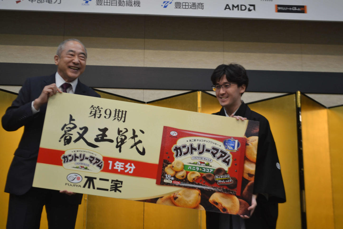 不二家の河村宣行社長（左）から贈られた副賞のカントリーマアム1年分の看板を手にする伊藤匠叡王（右）