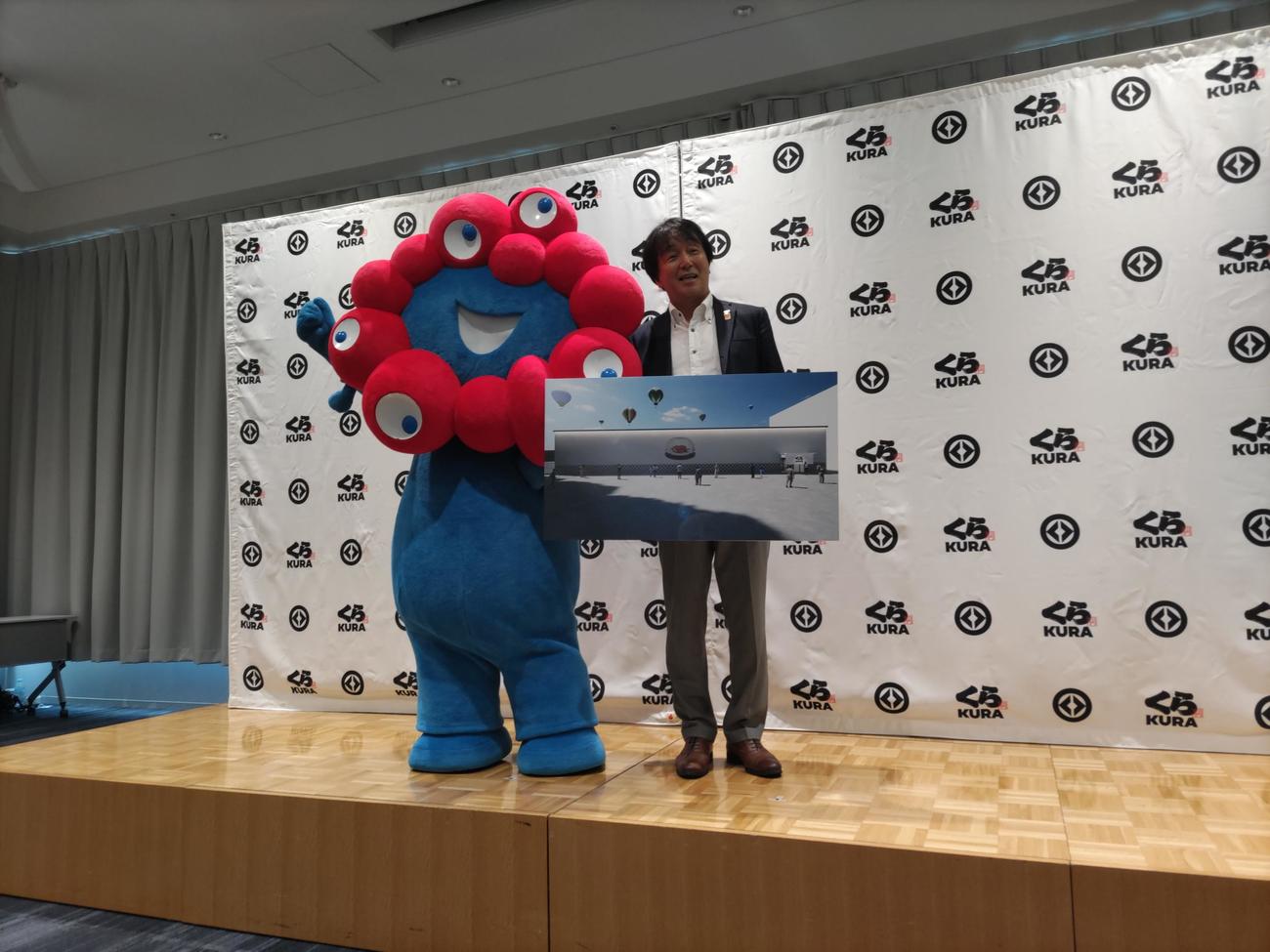 2025大阪・関西万博の出店説明会に登場した大阪・関西万博公式キャラクターミャクミャク（左）、くら寿司の岡本浩之取締役（撮影・松浦隆司）