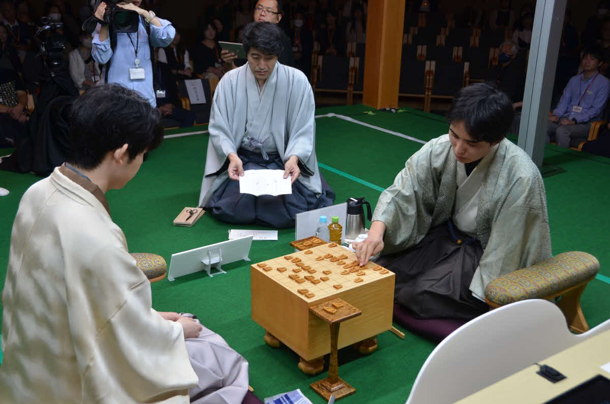 タイトル戦初登場で藤井聡太竜王（左）に挑戦する佐々木勇気八段（右）が立会人の森内俊之九段（中央）の開封した封じ手を指して竜王戦第1局の2日目が再開（日本将棋連盟提供）