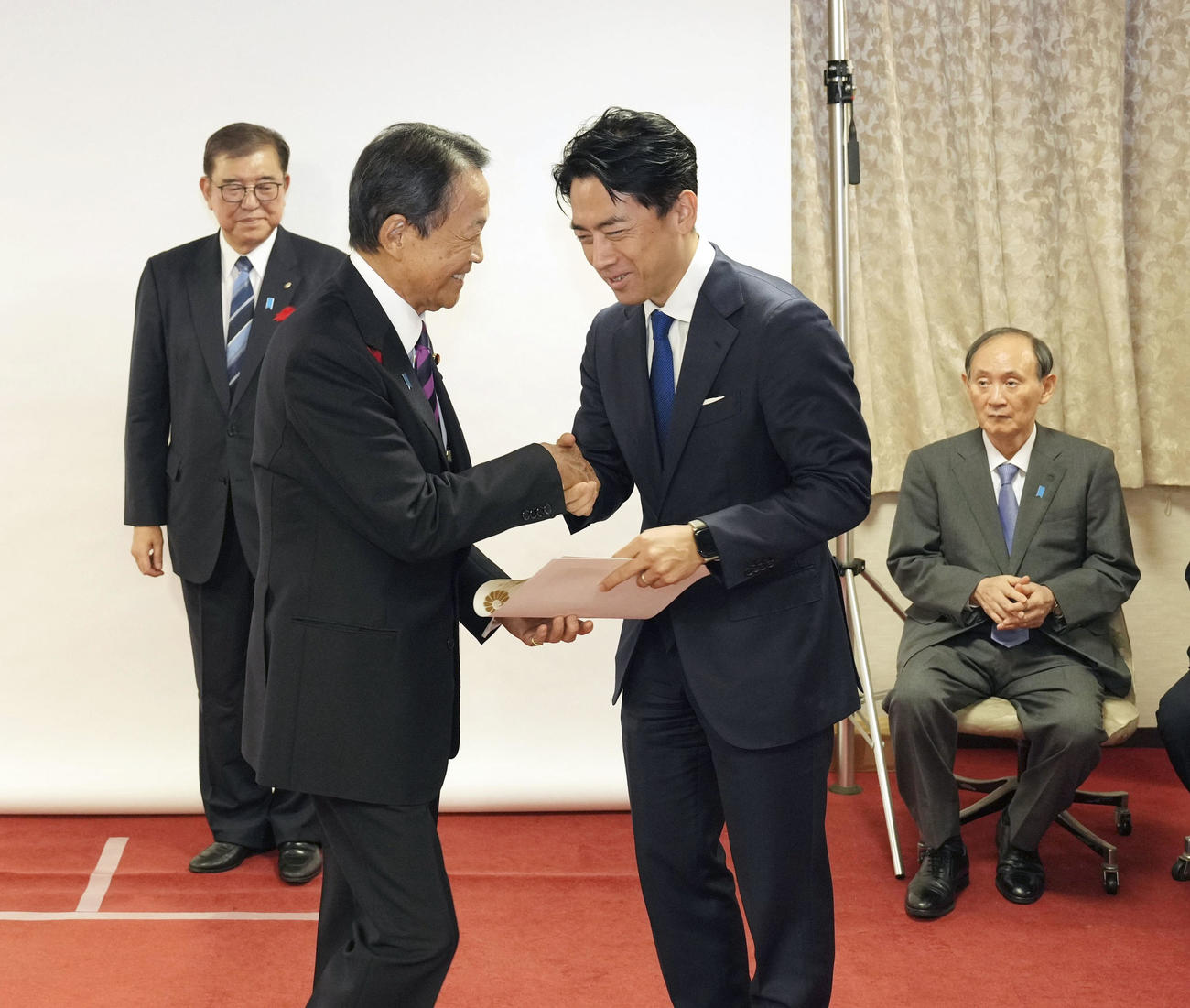 自民党本部で衆院選の公認証を交付された麻生最高顧問（左手前）と握手する小泉選対委員長。左奥は総裁の石破首相、右奥は菅副総裁（共同）