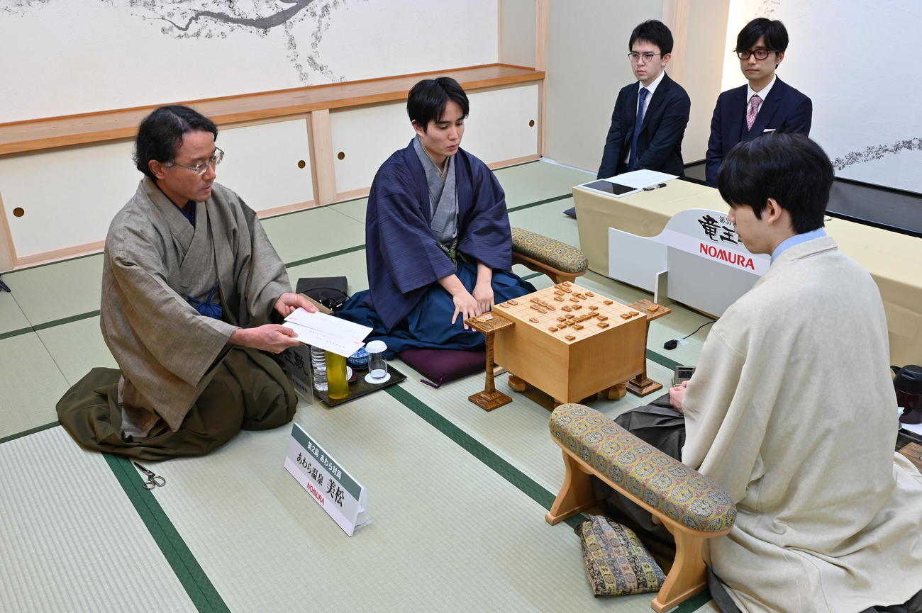 佐々木勇気八段（中央）の封じ手の封筒を示す立会人の深浦康市九段の手元を確認する藤井聡太竜王（右）（日本将棋連盟提供）