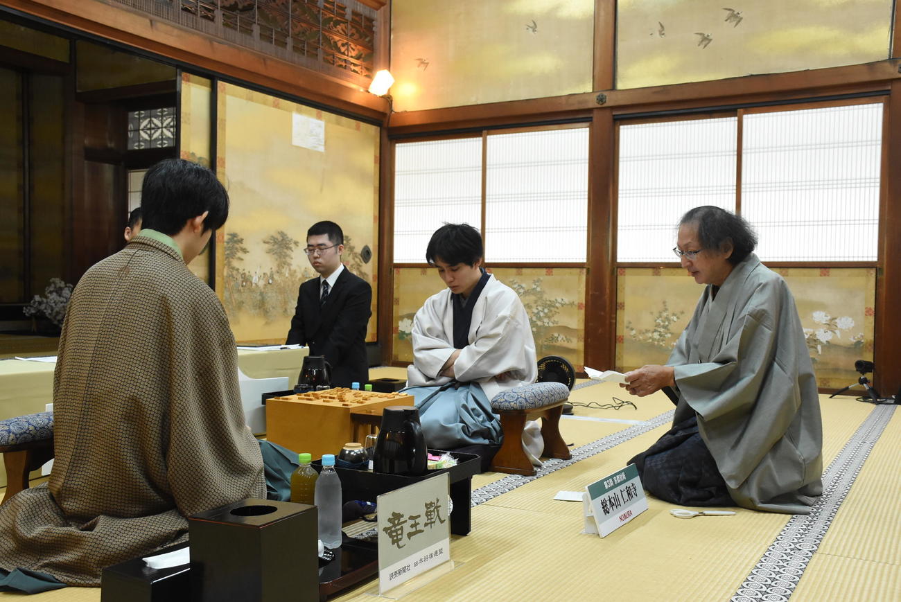 立会人の福崎文吾九段（右）が封じ手の封筒を開封し、読み上げを聞く佐々木勇気八段（中央）藤井聡太竜王（日本将棋連盟提供）
