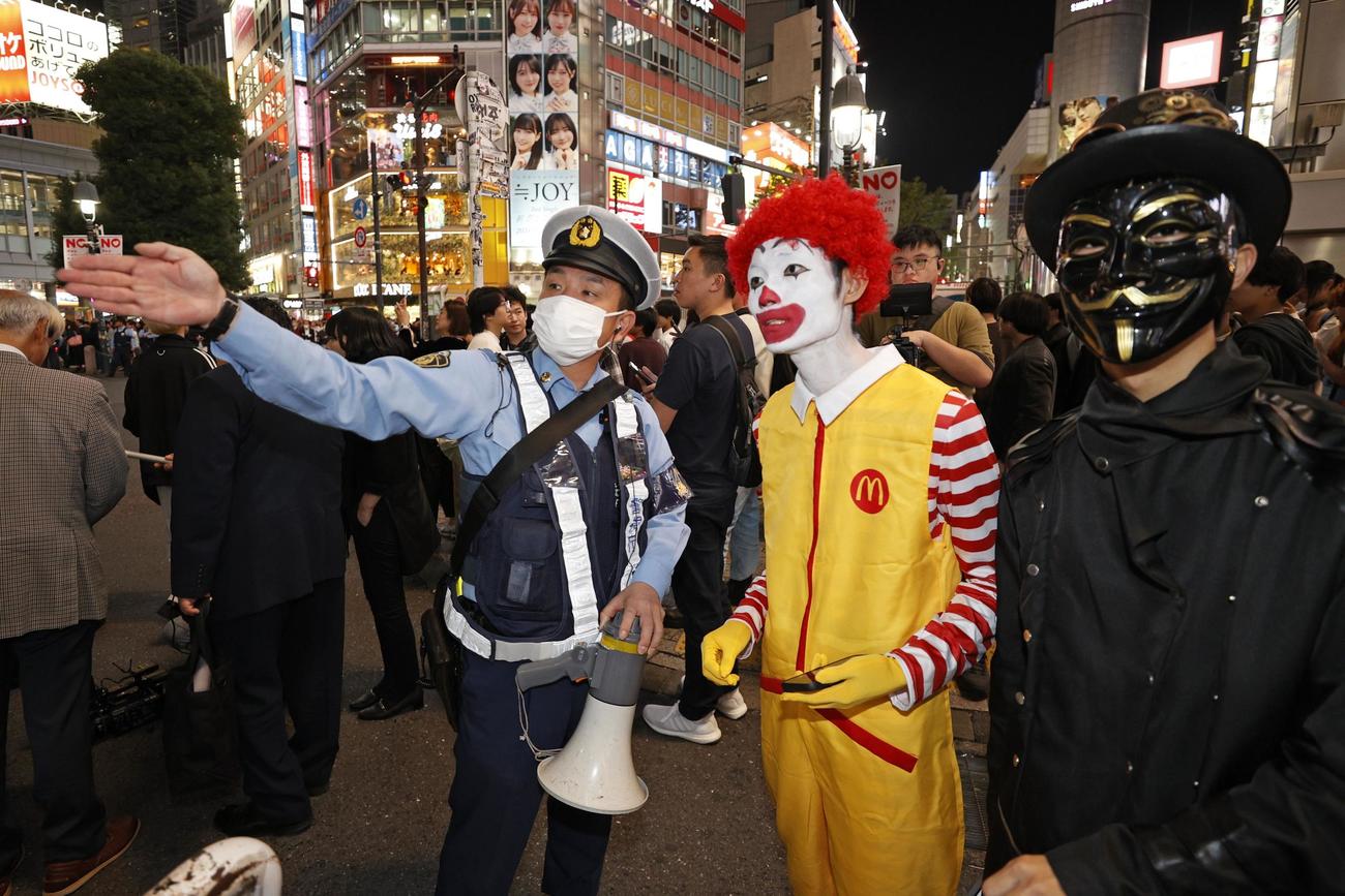 ハロウィーン当日を迎え、東京・渋谷のスクランブル交差点付近で仮装した人に道を問われる警察官（共同）