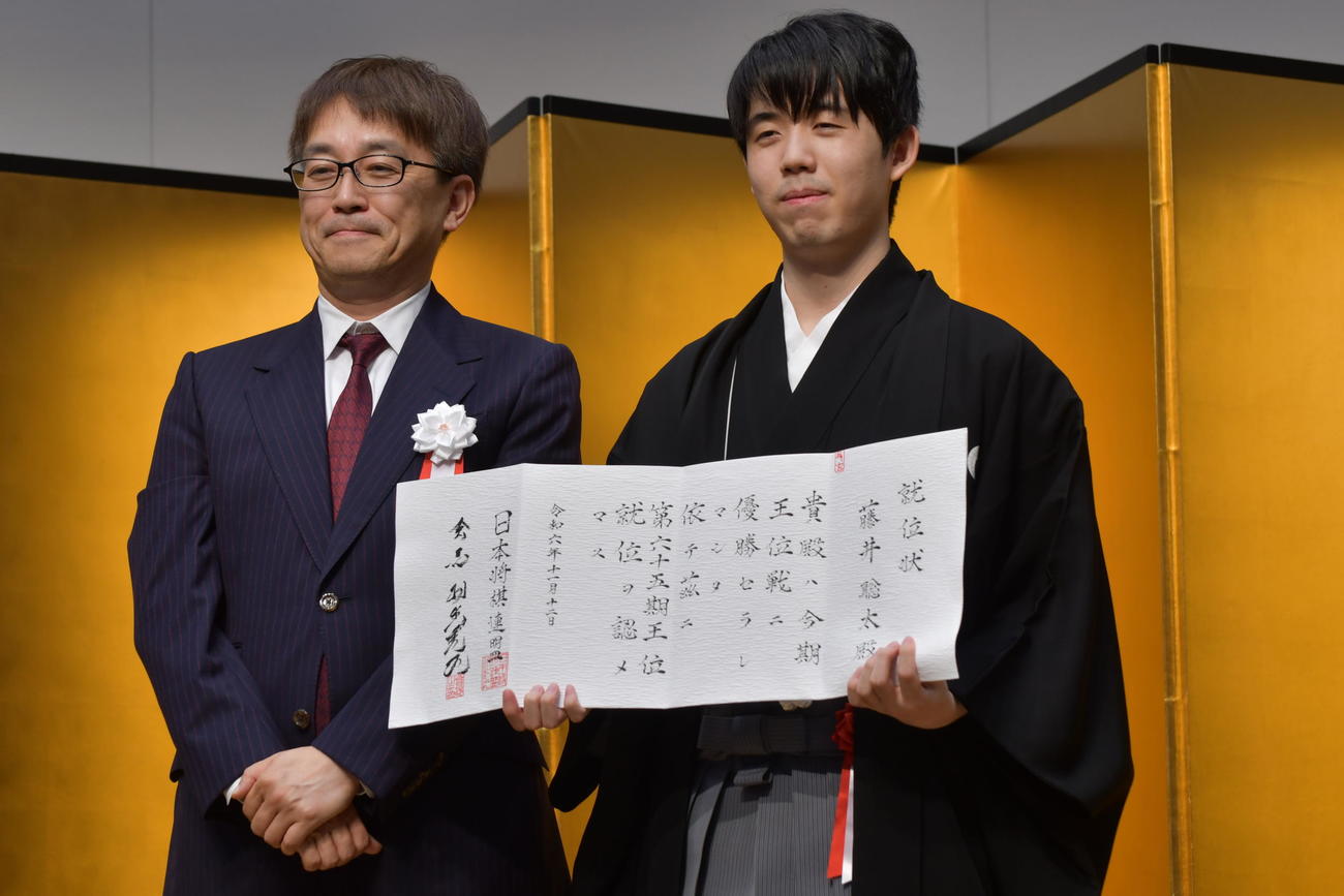 日本将棋連盟の羽生善治会長（左）から授与された就位状を手にする藤井聡太王位（右）