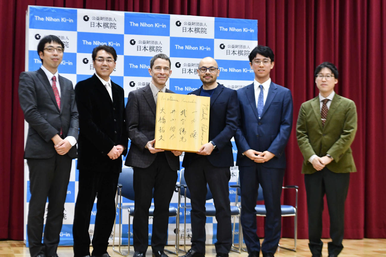 日本棋院来院記念の署名入り碁盤を手にするノーベル化学賞受賞者のデミス・ハサビス氏（右から3人目、左から大橋拓文七段、武宮陽光理事長、マイケル・レドモンド九段、1人おいて一力遼棋聖、井山裕太王座）