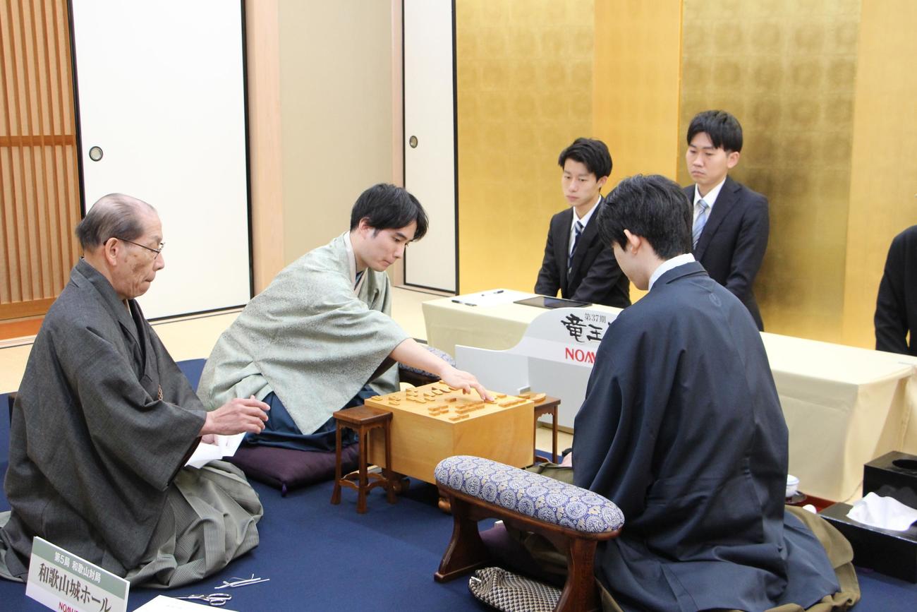 立会人の桐山清澄九段（左）が封じ手を読み上げ、駒を動かす佐々木勇気八段（中央）藤井聡太竜王（日本将棋連盟提供）
