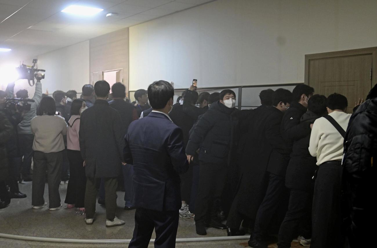 4日、ソウルの韓国国会内で、軍人らの突入を防ごうと壁を押さえる国会関係者ら（共同）