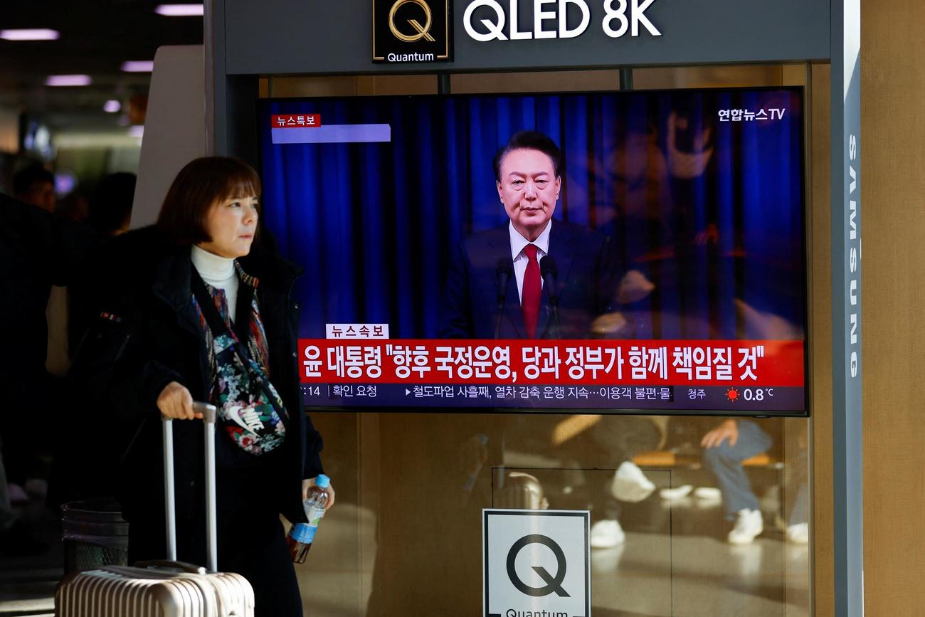 ソウルの駅で、韓国の尹錫悦大統領が国民に向けて演説するテレビ画面の前を通り過ぎる女性（ロイター）
