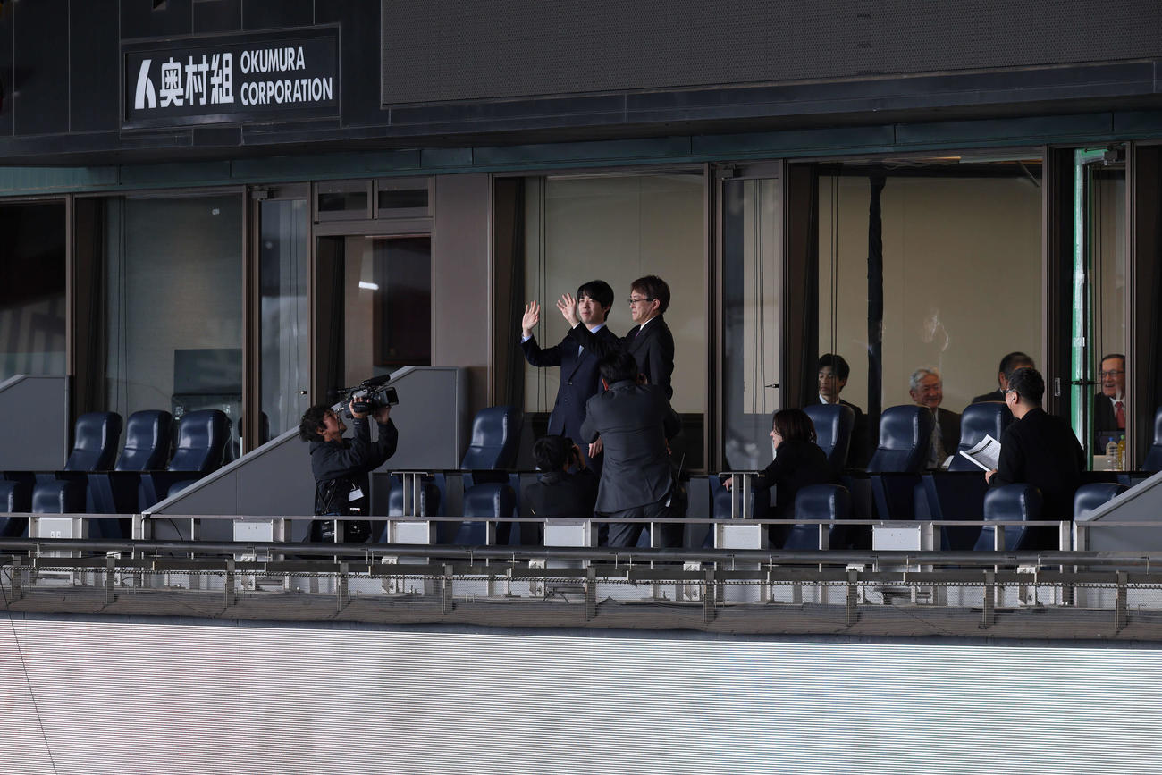 阪神甲子園球場での記念対局前に貴賓室のテラス席に登場し、手を振る日本将棋連盟会長の羽生善治九段（右）藤井聡太7冠（阪神甲子園球場提供）
