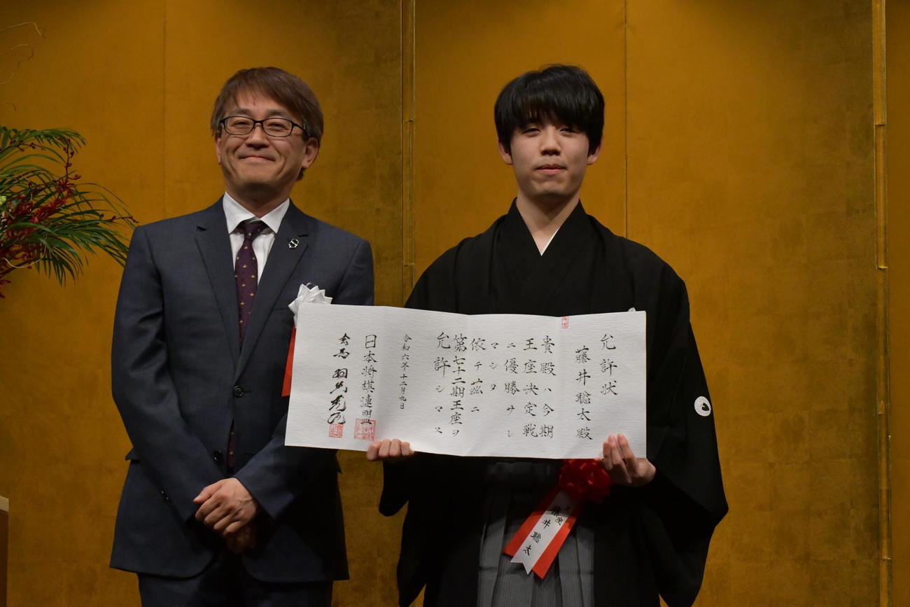 前日甲子園球場で記念他局を行った日本将棋連盟会長の羽生善治九段（左）から渡された允許（いんきょ）状を手にツーショットの撮影に応じた藤井聡太王座