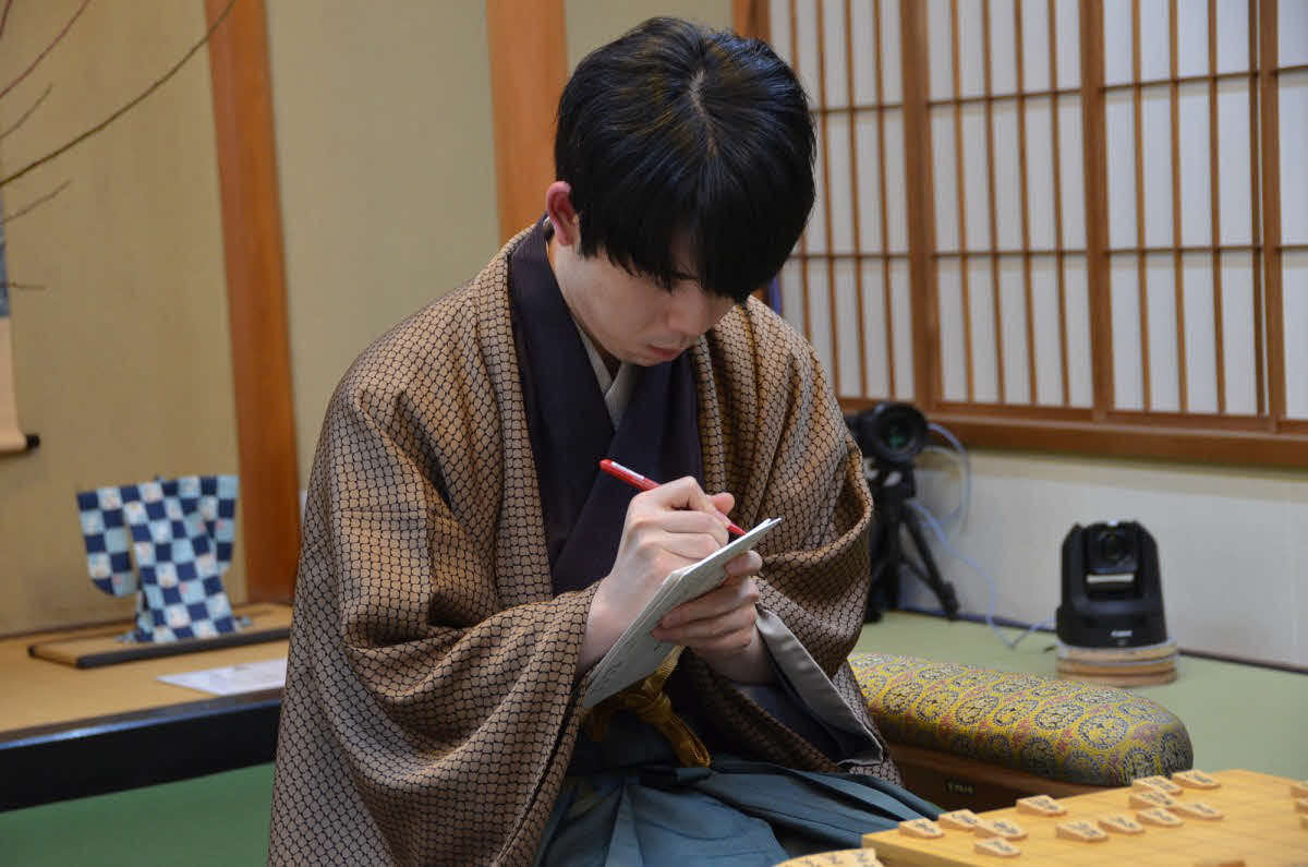 封じ手の入った封筒に署名する藤井聡太王将（日本将棋連盟提供）