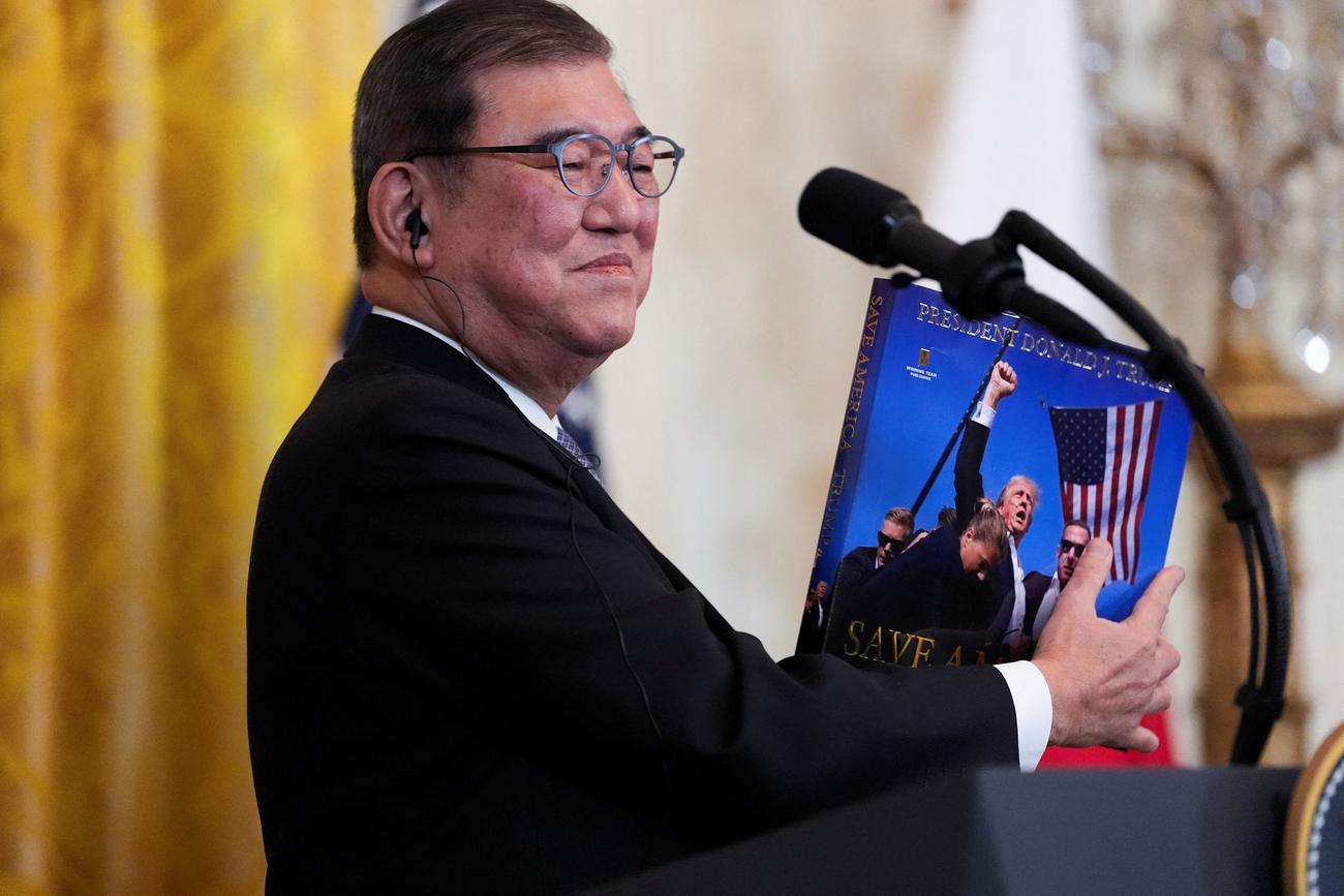 ホワイトハウスで乃記者会見で、ドナルド・トランプ大統領から贈られたプレゼントを見せる石破茂首相（２０２５年２月７日、ロイター）