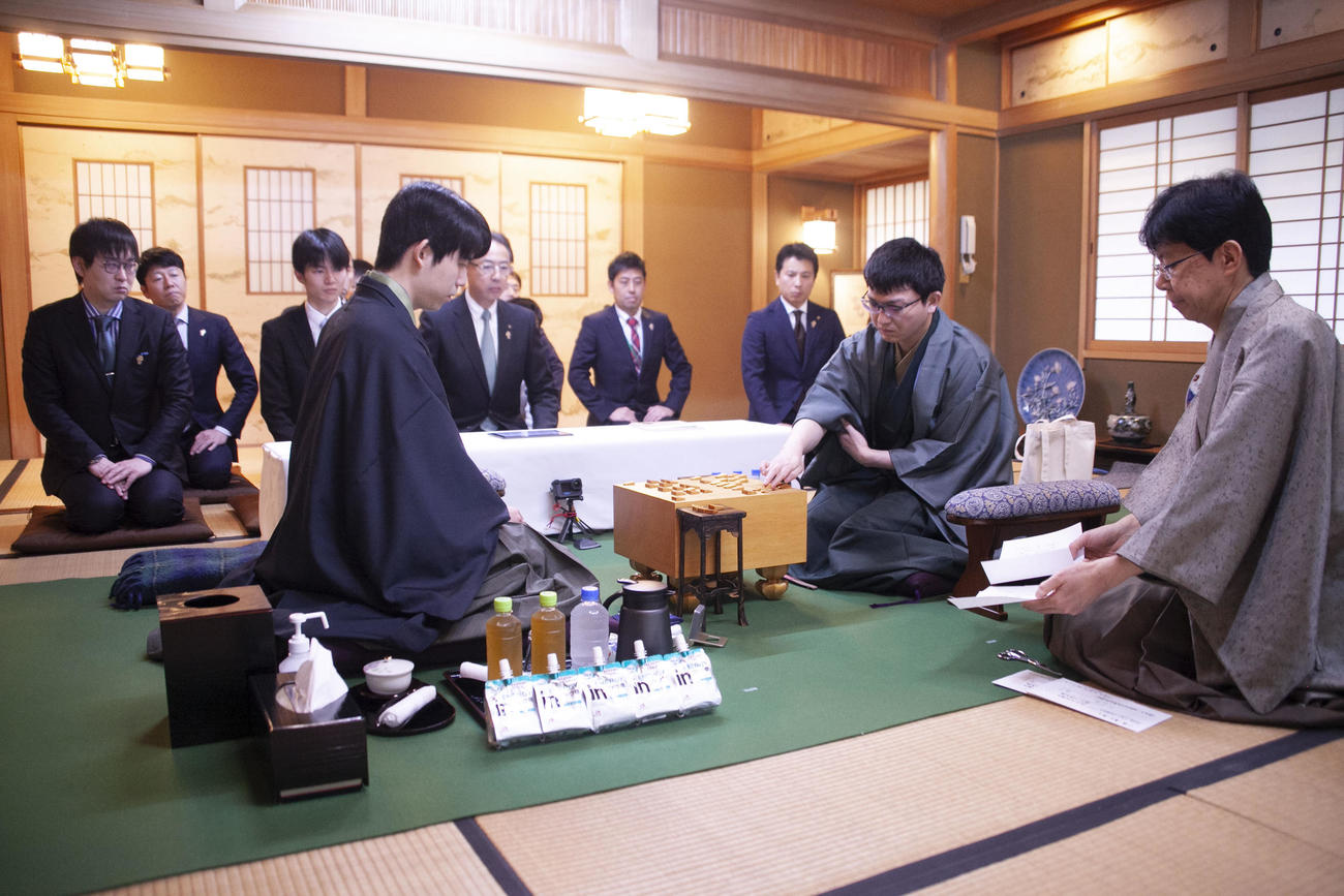 王将戦2日目　立会人の谷川浩司17世名人（右）が封じ手を読み上げ、封じ手を指す永瀬拓矢九段（中央）、左は藤井聡太王将（日本将棋連盟提供）